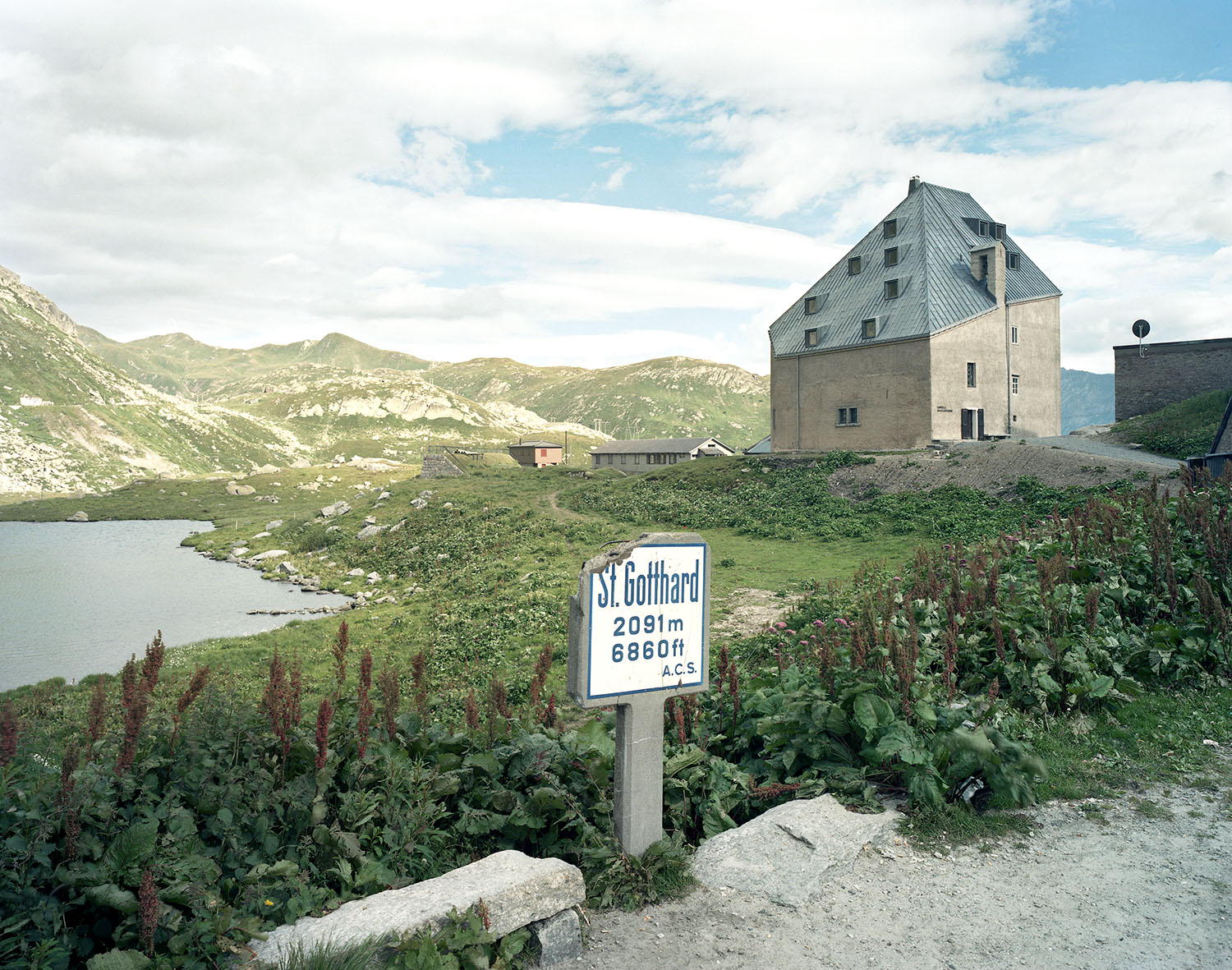 Old hospice, St. Gotthard Pass by Miller & Maranta — The hospice occupies a commanding position above a glacial lake, its cream-rendered stone walls and lead-clad mansard roof dominating the alpine valley.