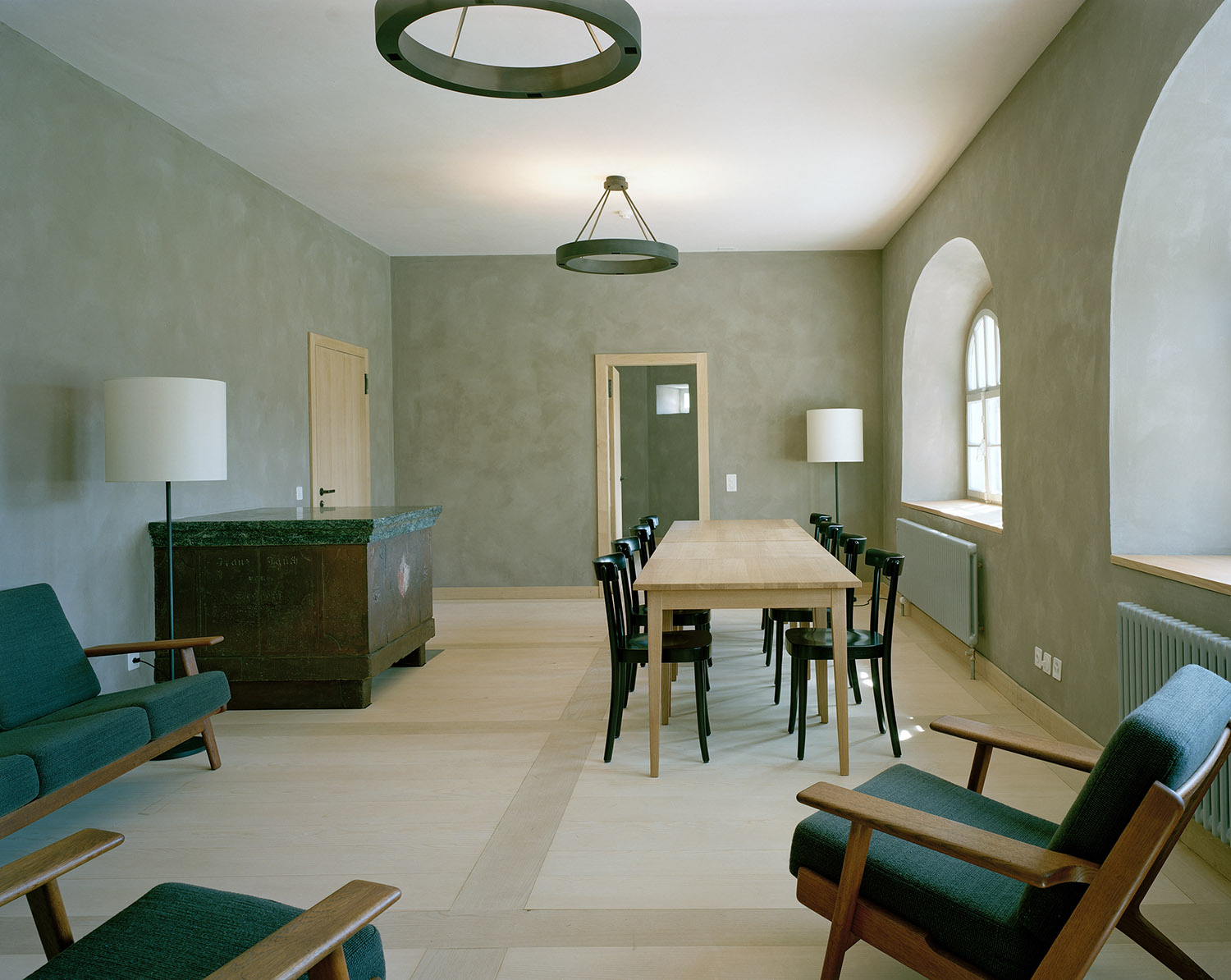 Old hospice, St. Gotthard Pass by Miller & Maranta — Interior of the restored hospice dining hall featuring a linear timber table with black spindle-back chairs arranged for communal seating.
