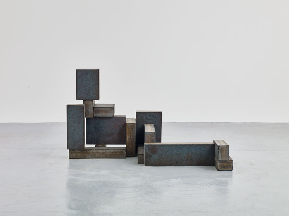 Sculptures by Antony Gormley — Antony Gormley's sculptural composition assembles weathered steel and bronze blocks in a cascading, stepped arrangement across a polished concrete floor.