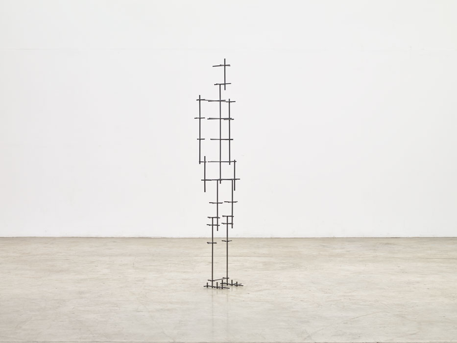 Sculptures by Antony Gormley — Antony Gormley constructs a vertical figure from stacked timber blocks of graduated sizes, each element marked with small perpendicular crosshatches.
