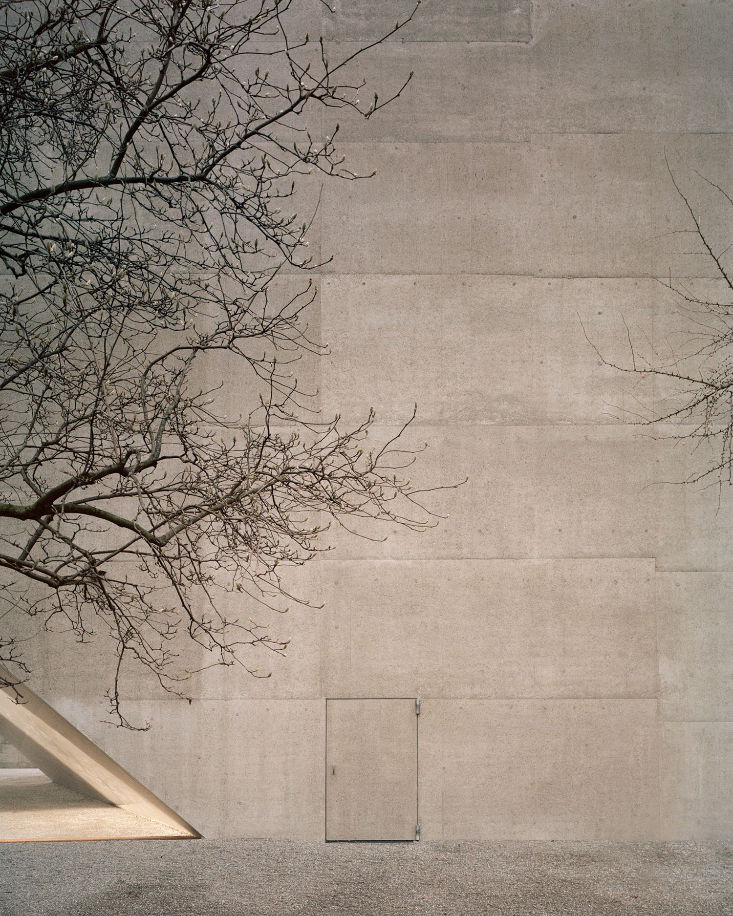 Swiss National Museum by Christ & Gantenbein photographed by Rory Gardiner — A cream-colored concrete facade dominates the frame, its smooth surface interrupted only by a small rectangular opening near the base.