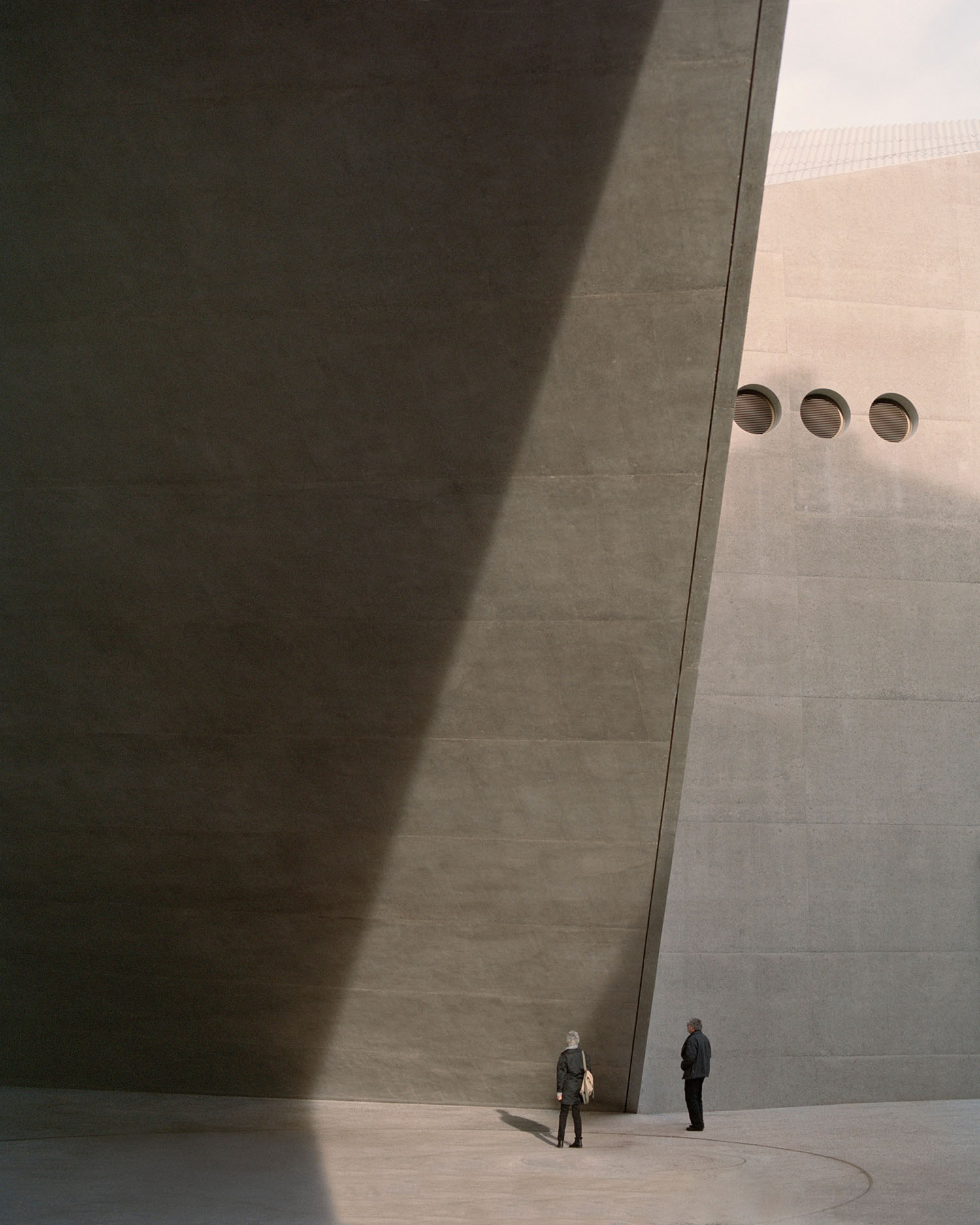 Swiss National Museum by Christ & Gantenbein photographed by Rory Gardiner — Two figures stand in the vast paved courtyard of Christ & Gantenbein's Swiss National Museum extension, dwarfed by the monumental cream-colored concrete facade.