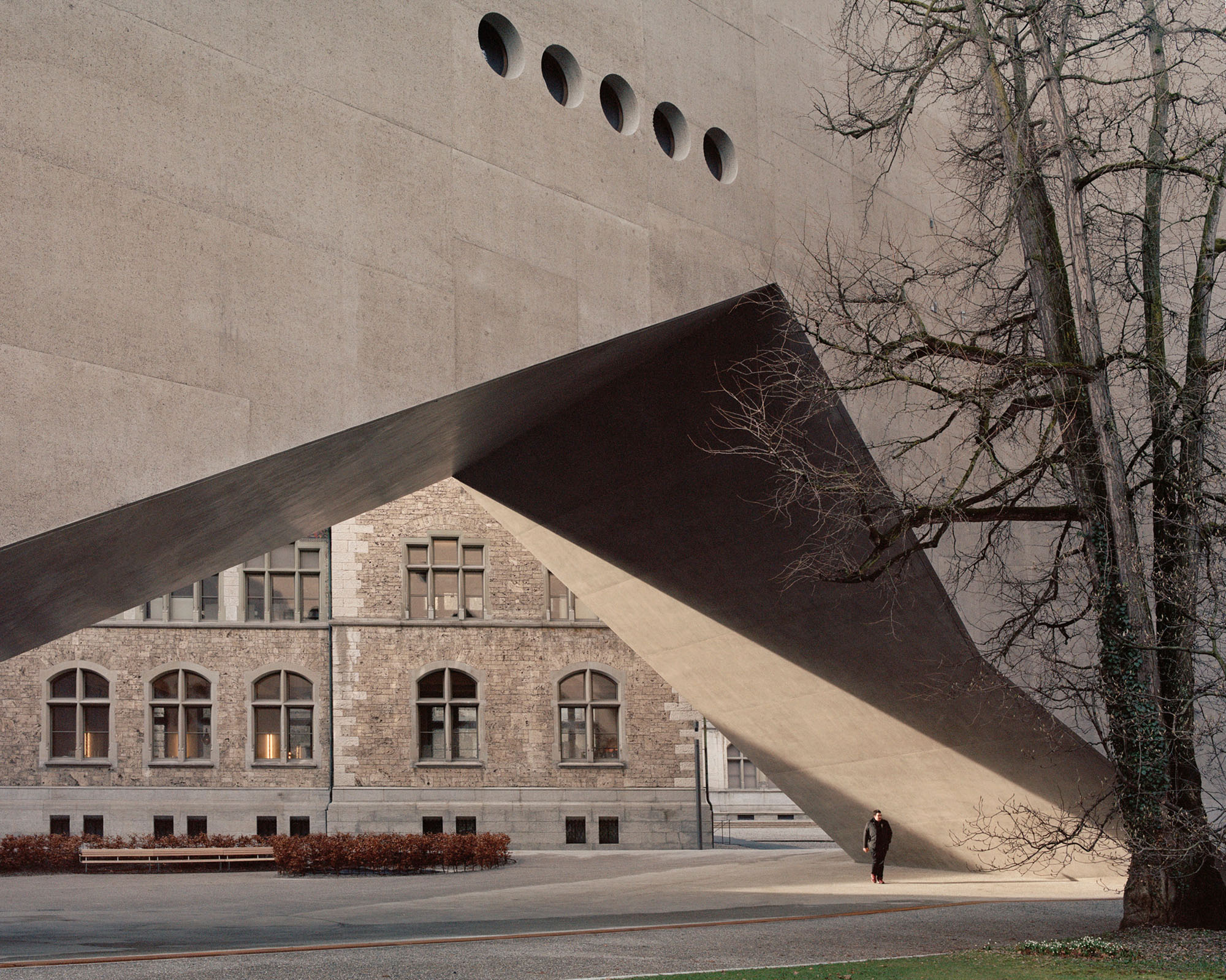 Swiss National Museum by Christ & Gantenbein photographed by Rory Gardiner — A monolithic cream-colored concrete wing extends dramatically across the frame, its pyramidal roof form echoing the stepped gable of the adjacent historic...