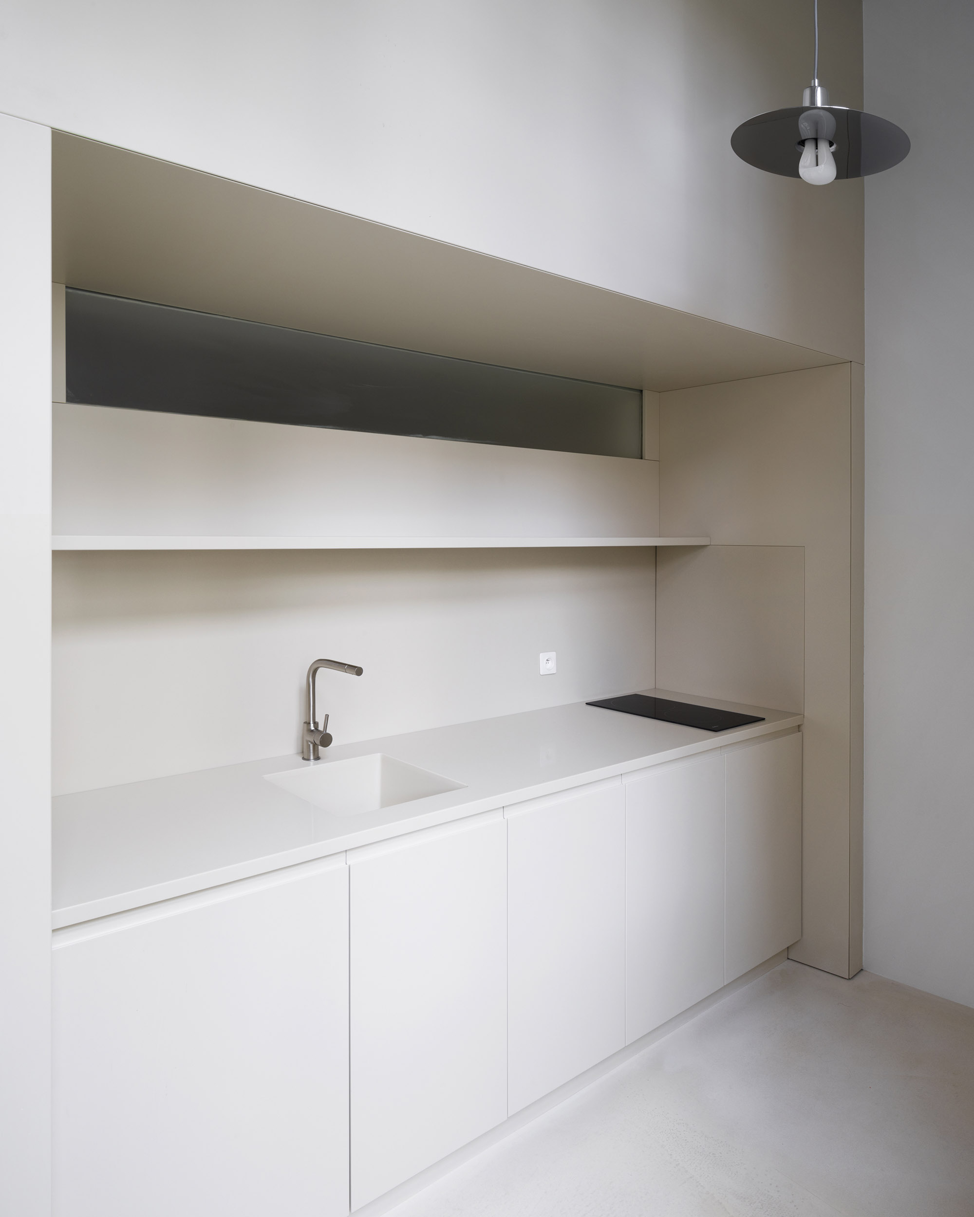 A-PLACE K907 by Thisispaper Studio — A galley kitchen carved from the K907 mezzanine interior features a continuous white plywood counter with integrated sink and black cooktop surface.
