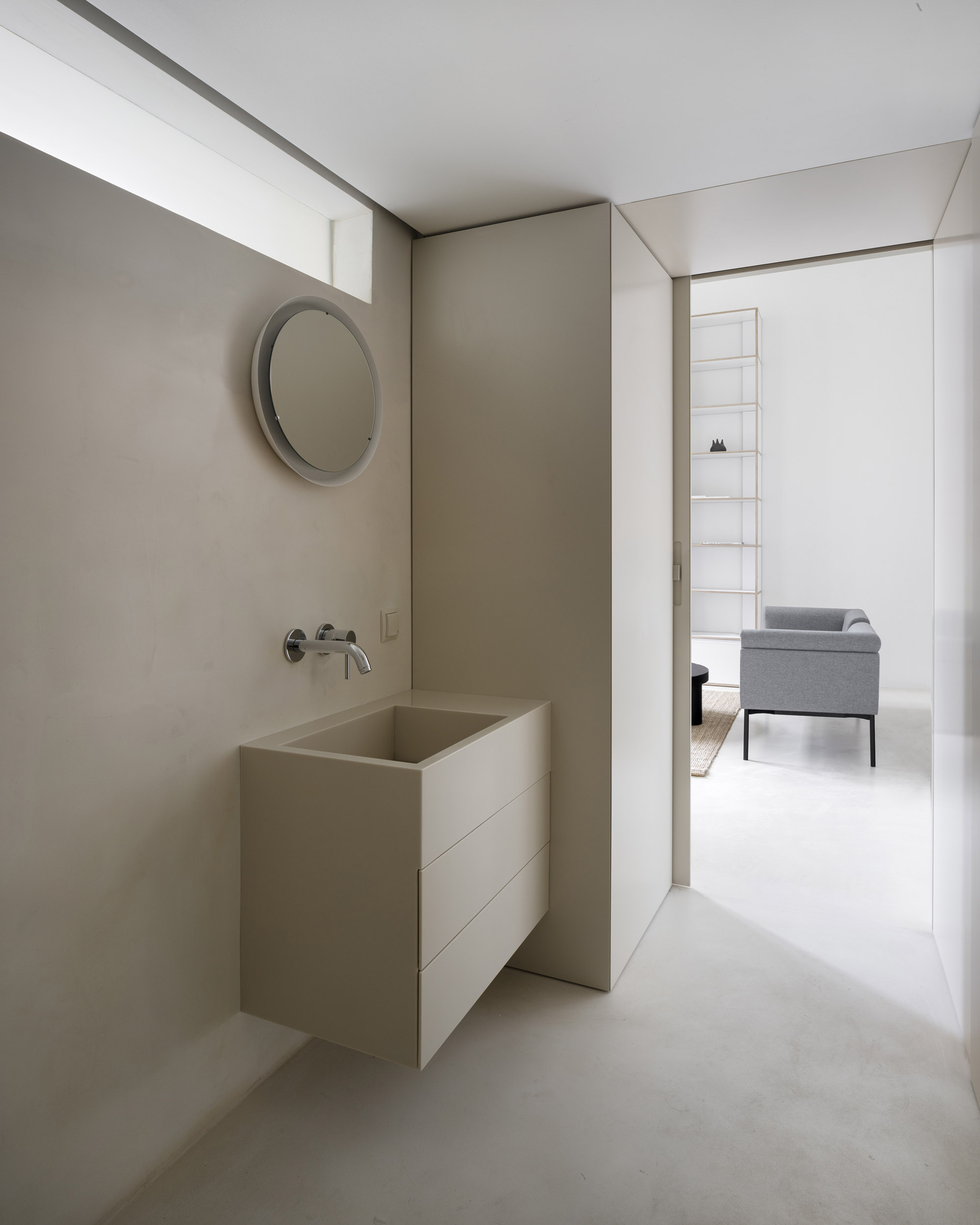 A-PLACE K907 by Thisispaper Studio — A bathroom alcove within the renovated 1903 Print House features a minimalist plywood vanity with two horizontal drawers positioned beneath a circular mirror.