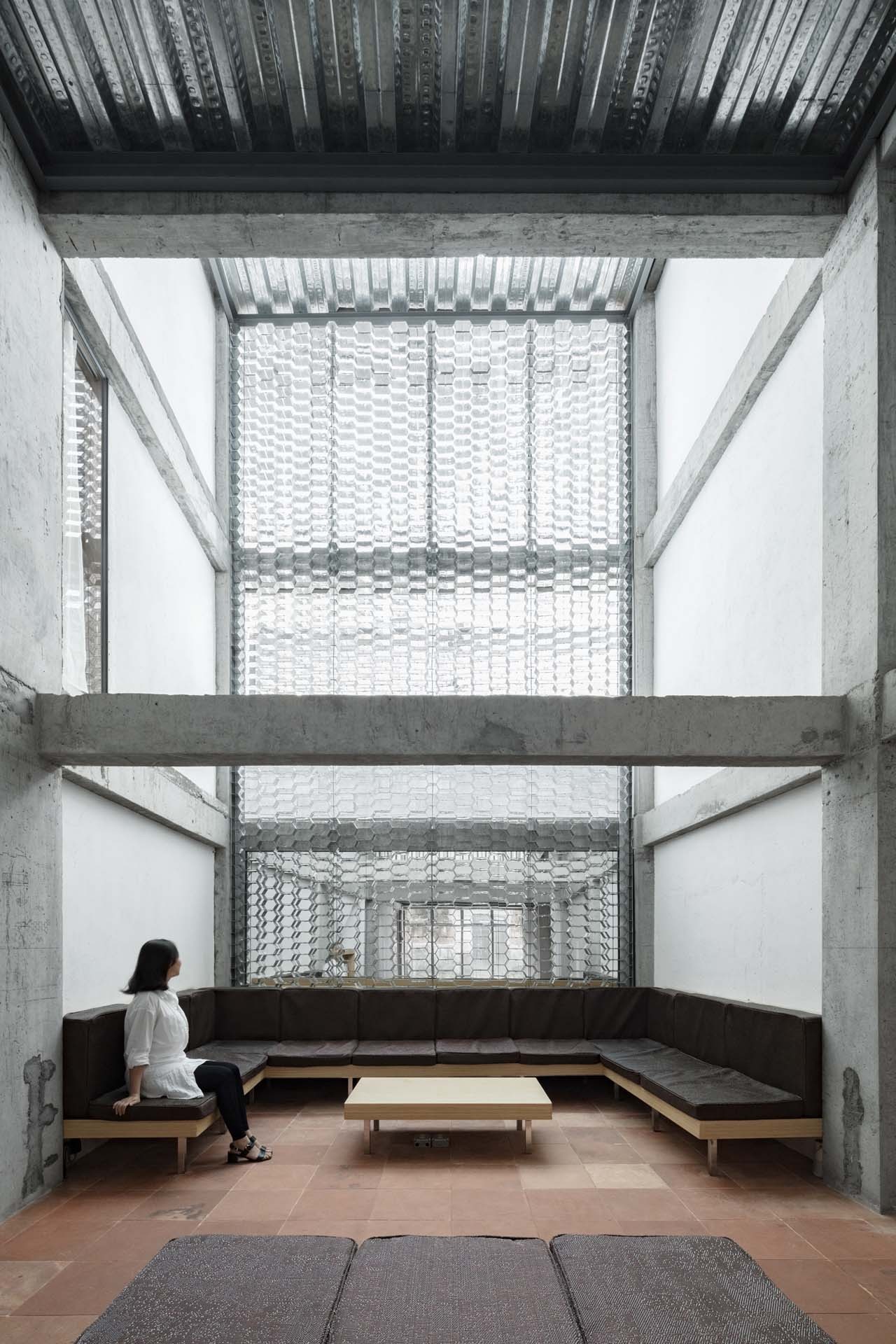 Hotel Far & Near Nanhao St. by kooo architects — A sectional interior view of Hotel Far & Near's communal lounge, showing the stripped concrete structural frame creating a dramatic vertical threshold.