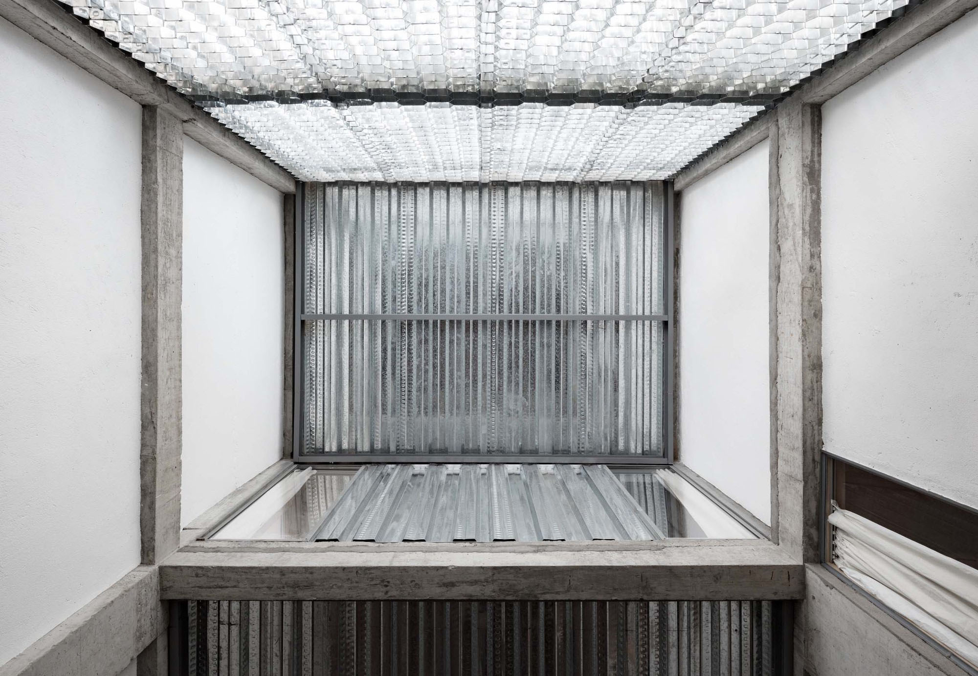 Hotel Far & Near Nanhao St. by kooo architects — A concrete threshold portal frames a frosted channel glass partition wall, its vertical fluting creating uniform light diffusion across the glazed surface.