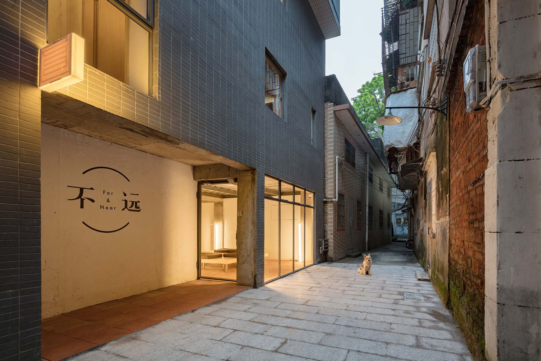 Hotel Far & Near Nanhao St. by kooo architects — A narrow alleyway entrance to Hotel Far & Near features a modern storefront with frosted channel glass panels set within an exposed concrete frame.