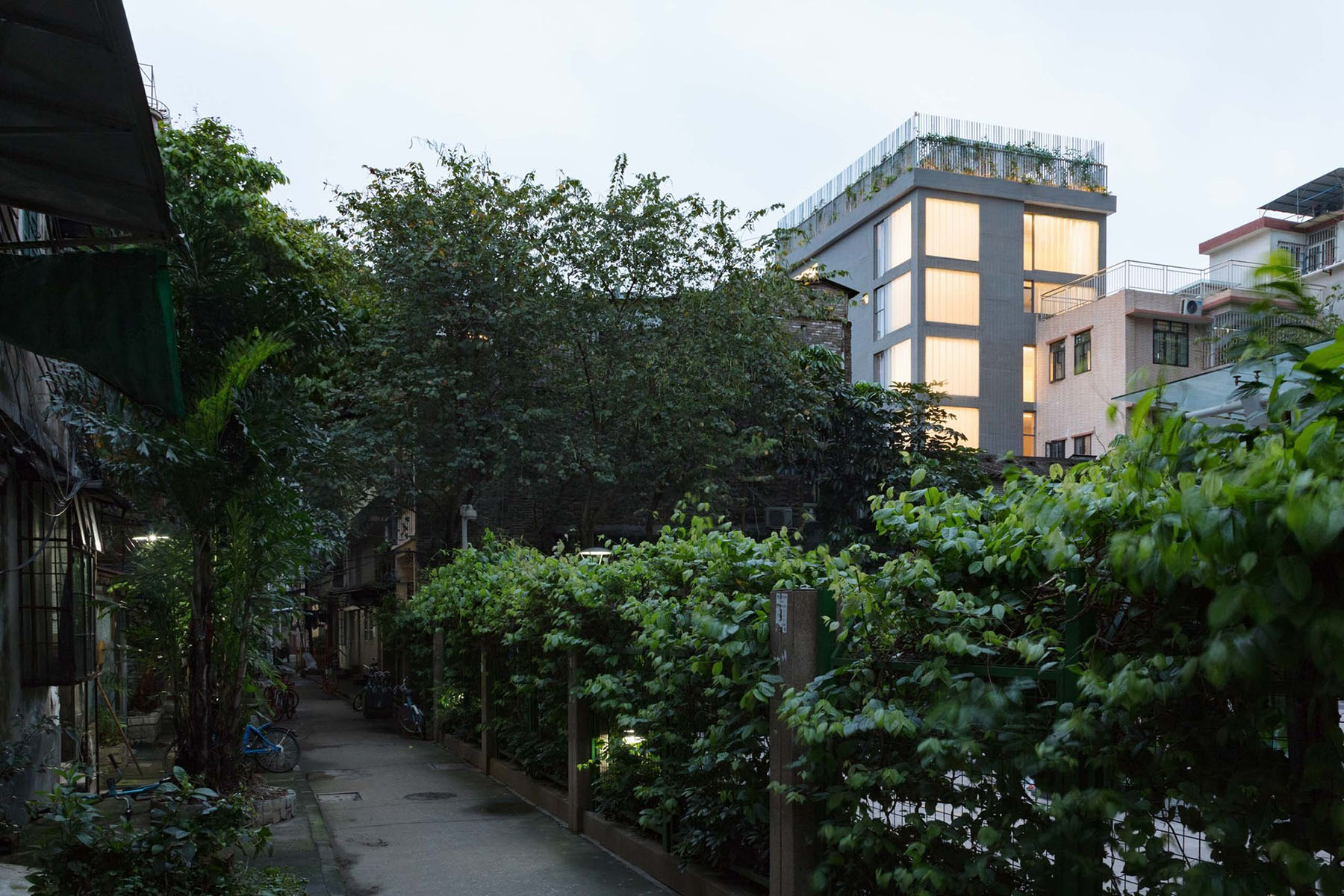 Hotel Far & Near Nanhao St. by kooo architects — A narrow passage between residential structures reveals the new Hotel Far & Near insertion rising behind dense vegetation.