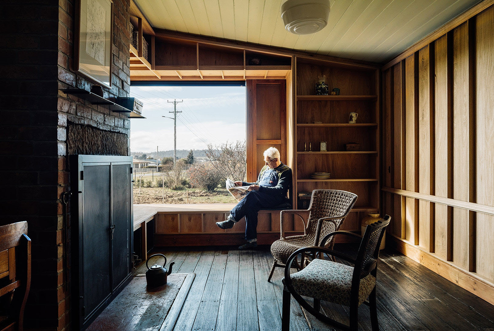 Bozen's Cottage by Taylor + Hinds Architects — A timber-lined interior space frames a view across rural landscape through a large horizontal window.