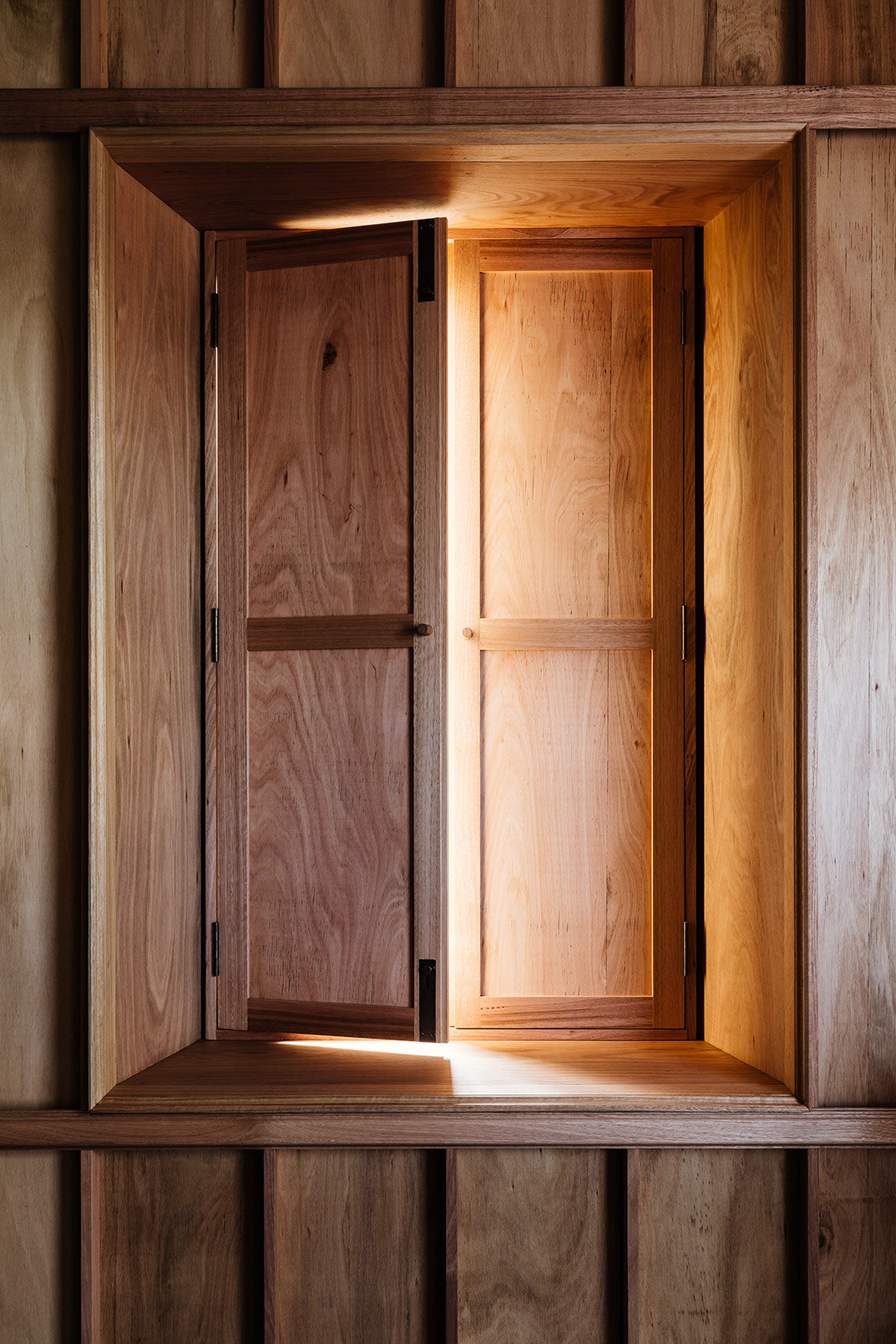 Bozen's Cottage by Taylor + Hinds Architects — A recessed timber-framed window aperture set within panelled wood wall exposes two wooden doors in contrasting tones.