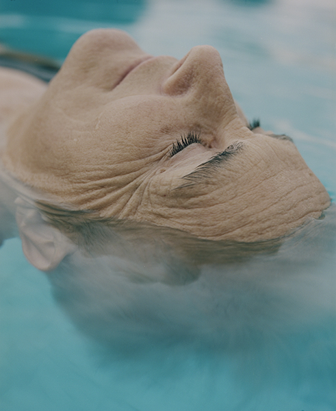 Selected works by András Ladocsi — A close-up portrait of a man's head tilted back and partially submerged in turquoise water, with the water line crossing at mouth level.
