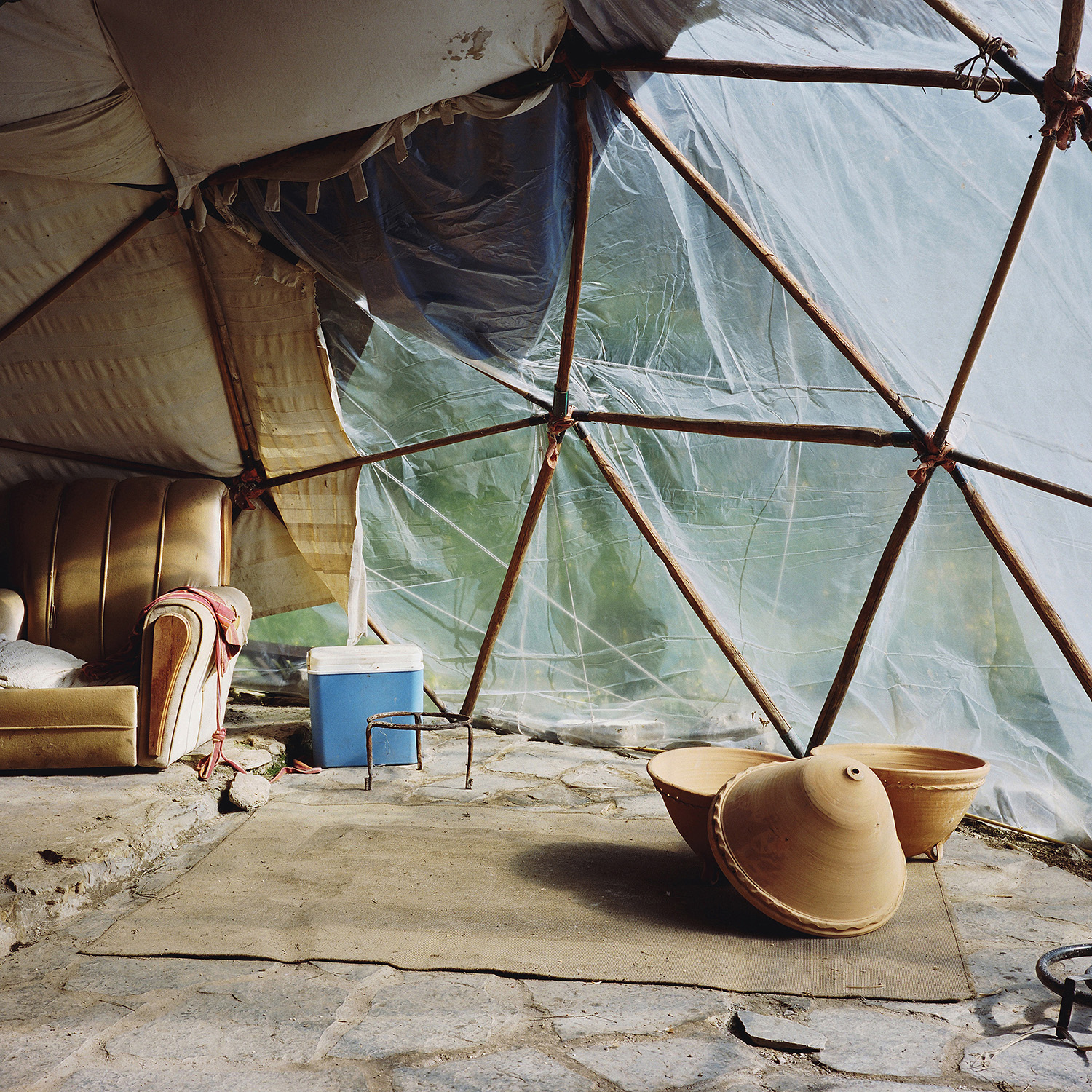 Scrublands by Antoine Bruy — Interior view of a transparent plastic-sheeted shelter supported by timber poles lashed with rope at structural joints.