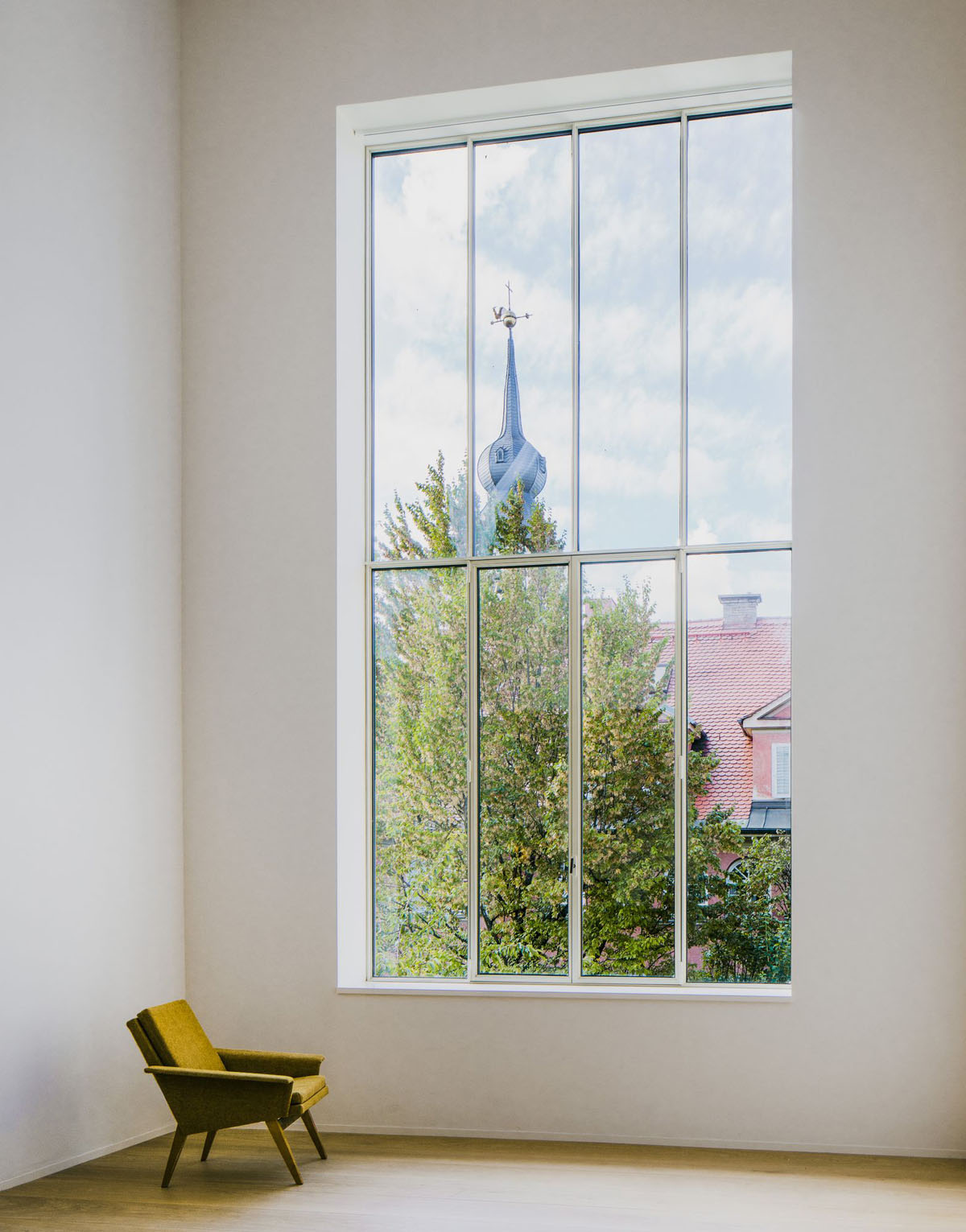 Bogenhausen House by David Chipperfield Architects — A gridded aluminum-framed window with eight panes dominates the white plaster interior wall, framing layered views of the landscape beyond: dense green...