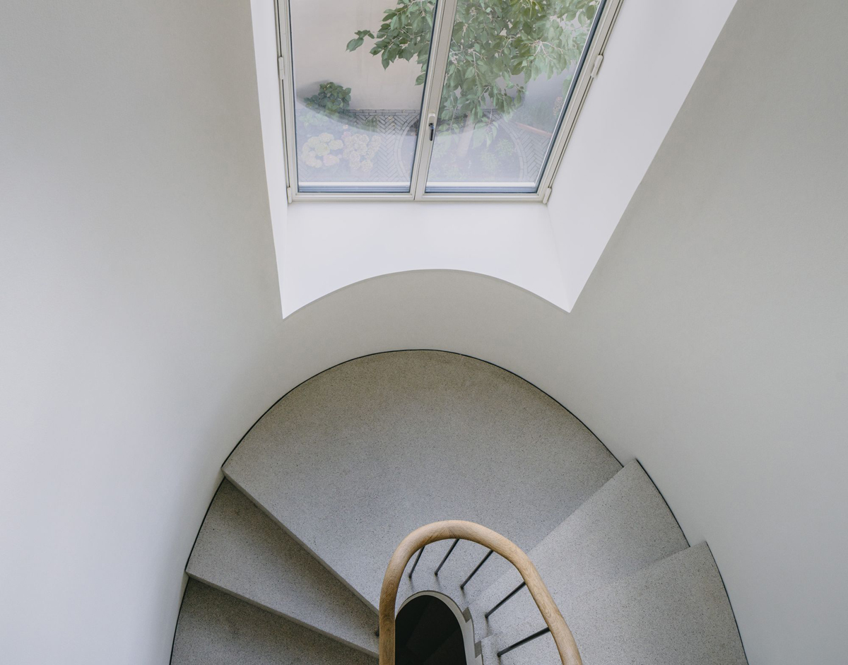 Bogenhausen House by David Chipperfield Architects — A spiral staircase photographed from above, its geometric progression anchored by a wooden handrail curving toward the center.