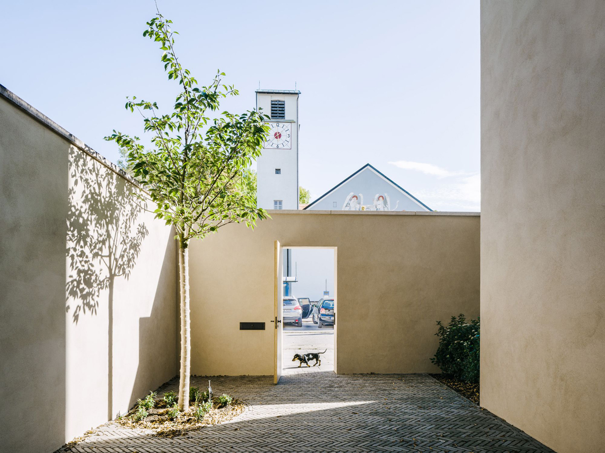 Bogenhausen House by David Chipperfield Architects — A rendered courtyard entrance framed by sand-colored walls creates a geometric passage toward the street.