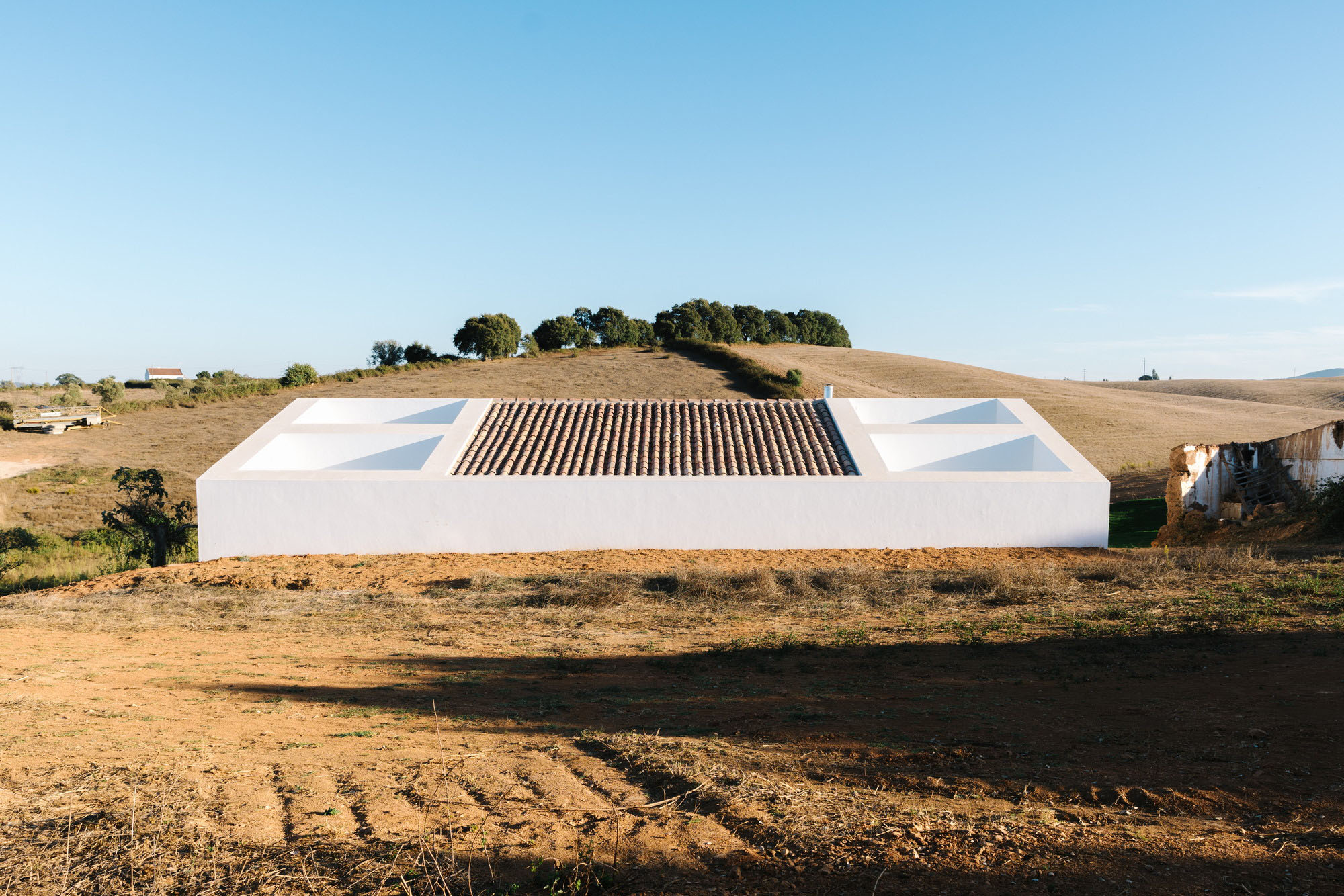 Cercal House by Atelier Data — Cercal House presents a rendered white facade with minimal fenestration, its horizontal massing aligned to the sloping terrain of Portugal's Alentejo region.