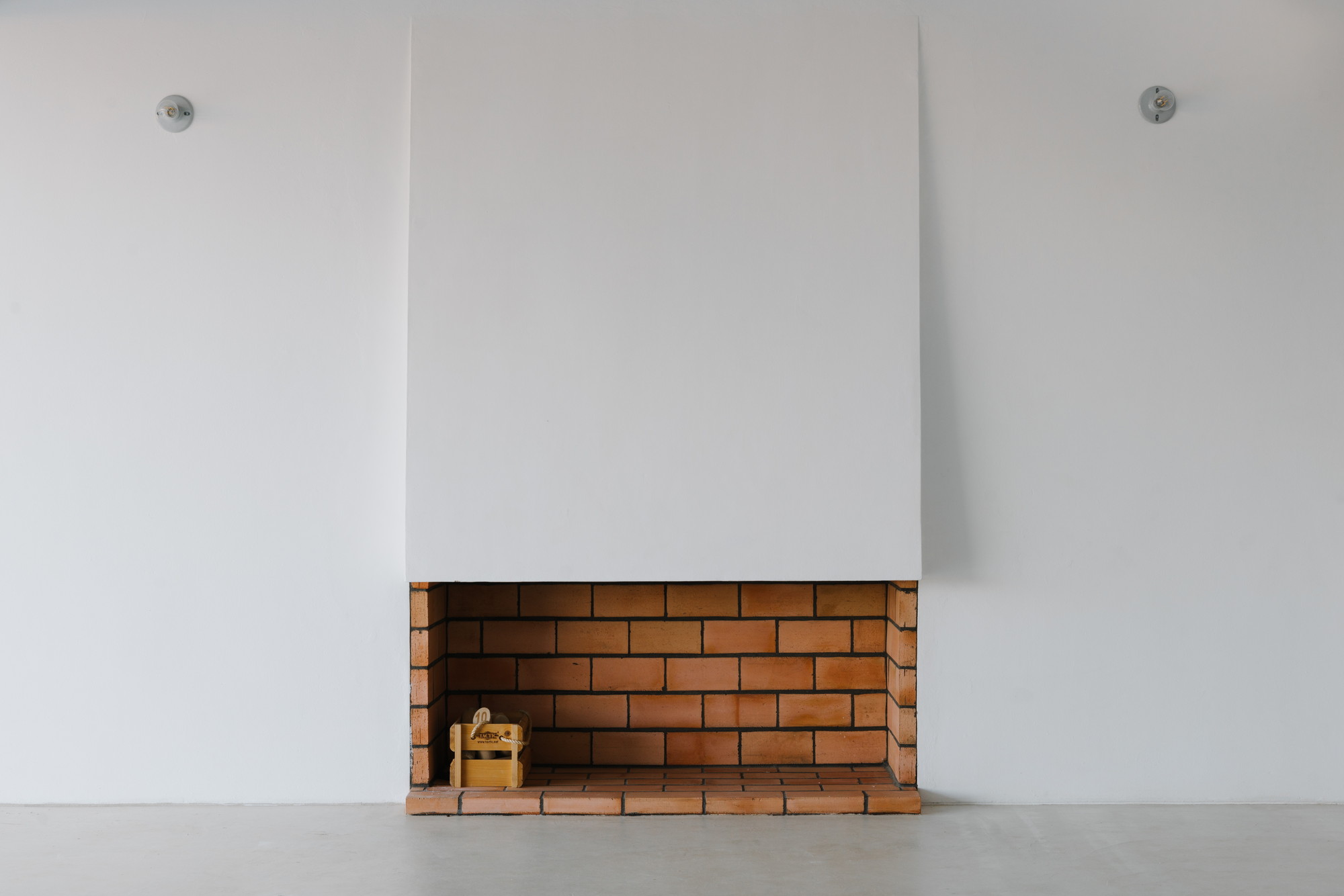 Cercal House by Atelier Data — A rendered white-wall interior elevation frames a recessed brick fireplace cavity with horizontal courses of terracotta-toned masonry.