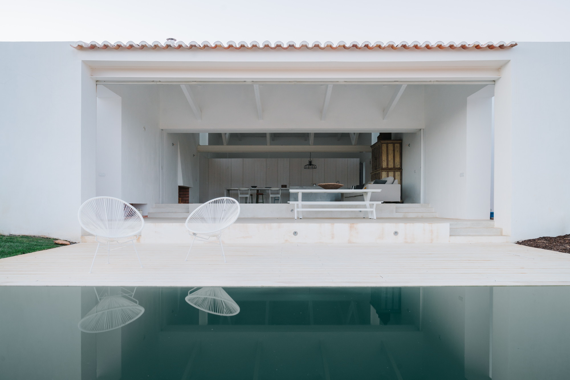 Cercal House by Atelier Data — The poolside facade of Cercal House presents a rendered white pavilion with horizontal massing that frames an open-plan interior.