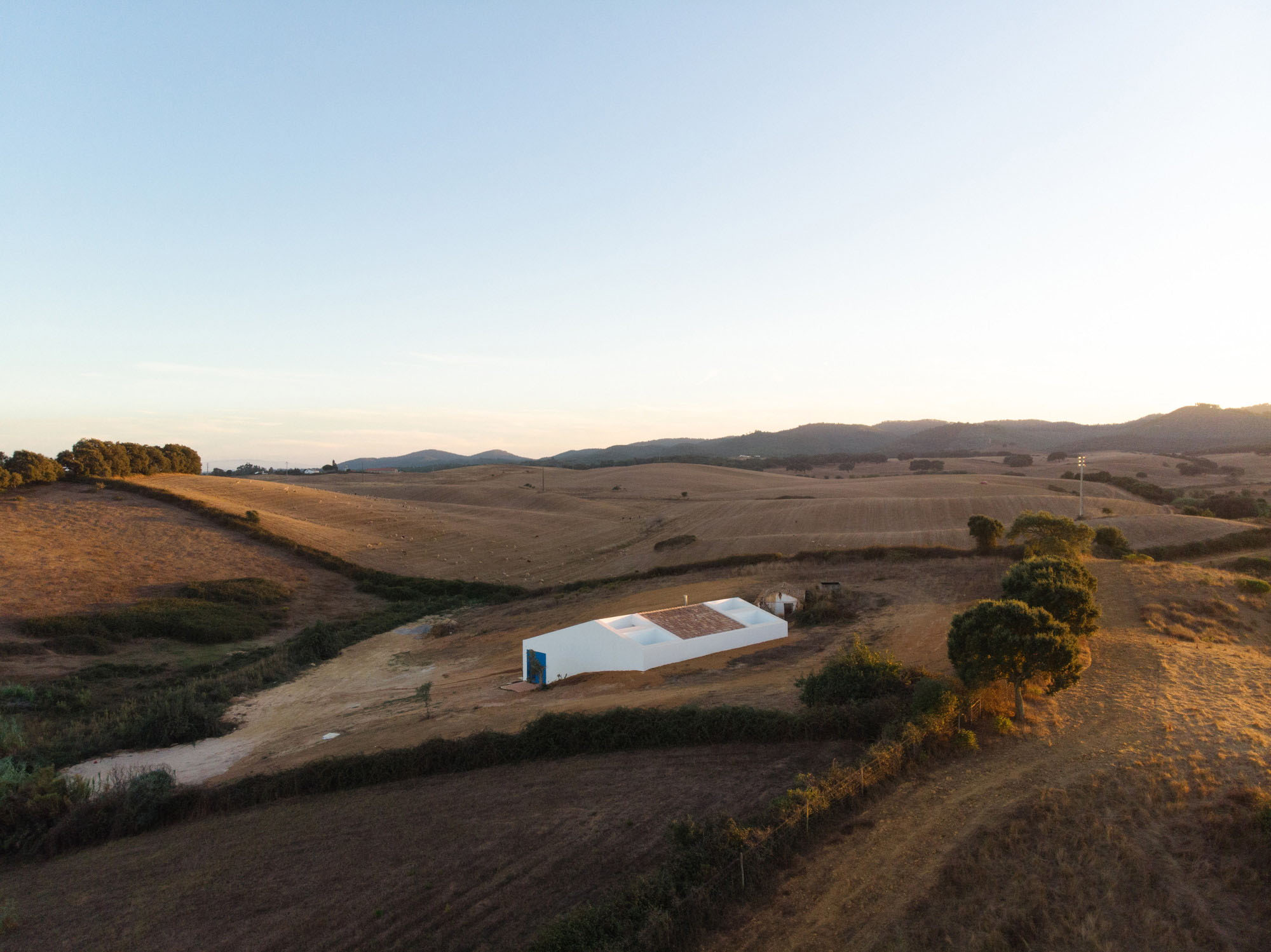 Cercal House by Atelier Data — Cercal House emerges from the rolling Alentejo landscape as a rendered white volume with dark pitched roof, its horizontal massing aligned with the valley's...