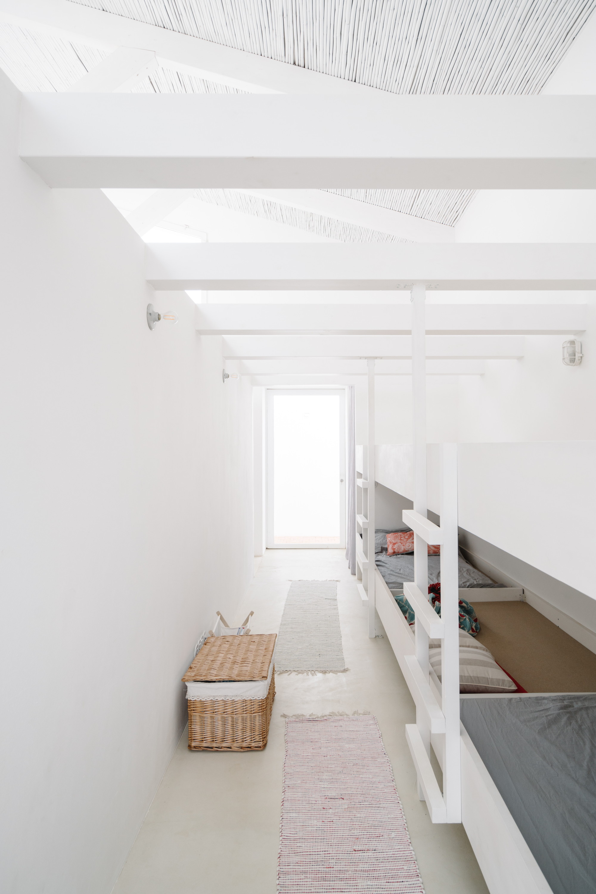 Cercal House by Atelier Data — A narrow corridor runs through a white-rendered attic space with exposed beam structure visible in the ceiling.