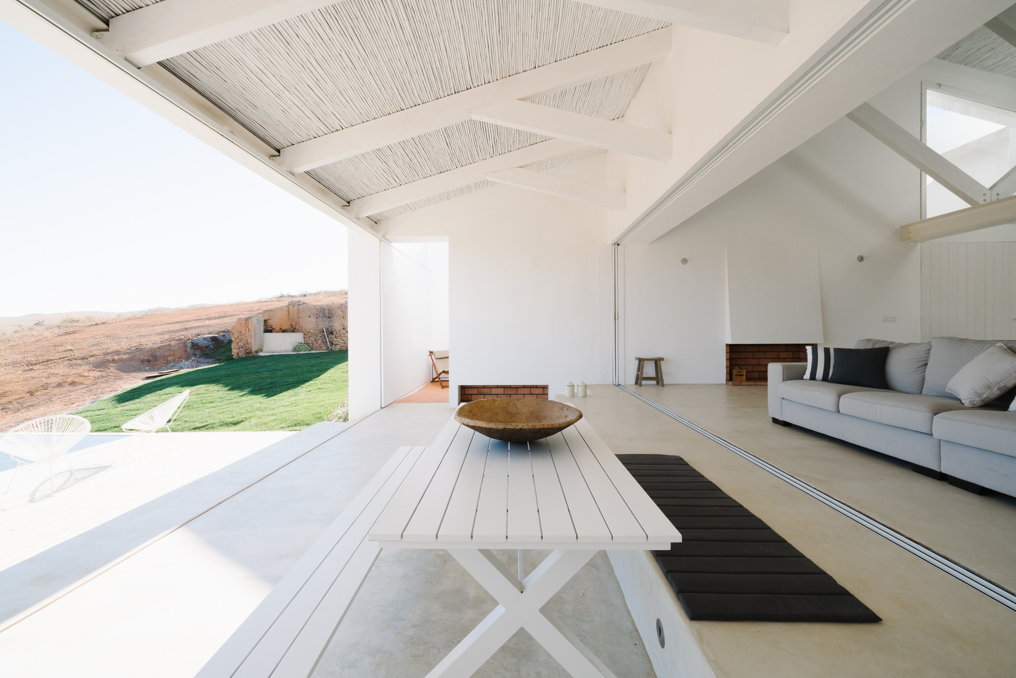 Cercal House by Atelier Data — The covered terrace frames a threshold between interior and landscape, with a white-rendered structural beam supporting the expansive overhang.