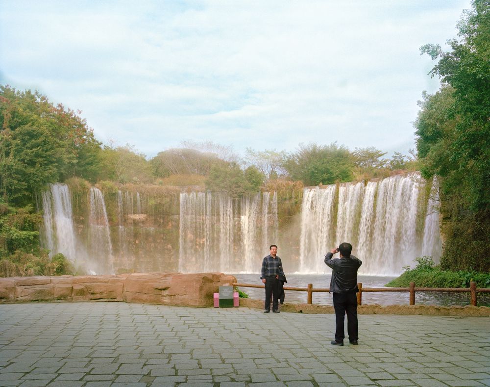 I am just a scenic spot by Pauilne Niks — A reconstructed waterfall landscape features multiple vertical stone curtain walls cascading across a wide patio.