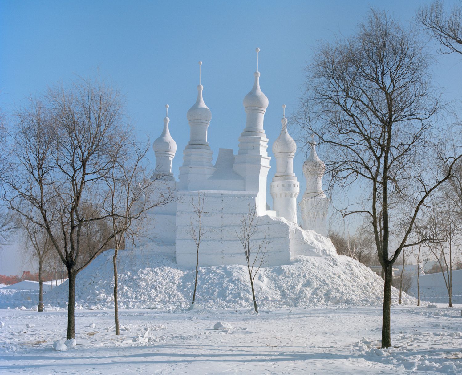 I am just a scenic spot by Pauilne Niks — A white onion-domed Orthodox church structure stands on an elevated mound of compacted snow and earth, surrounded by bare deciduous trees planted in...