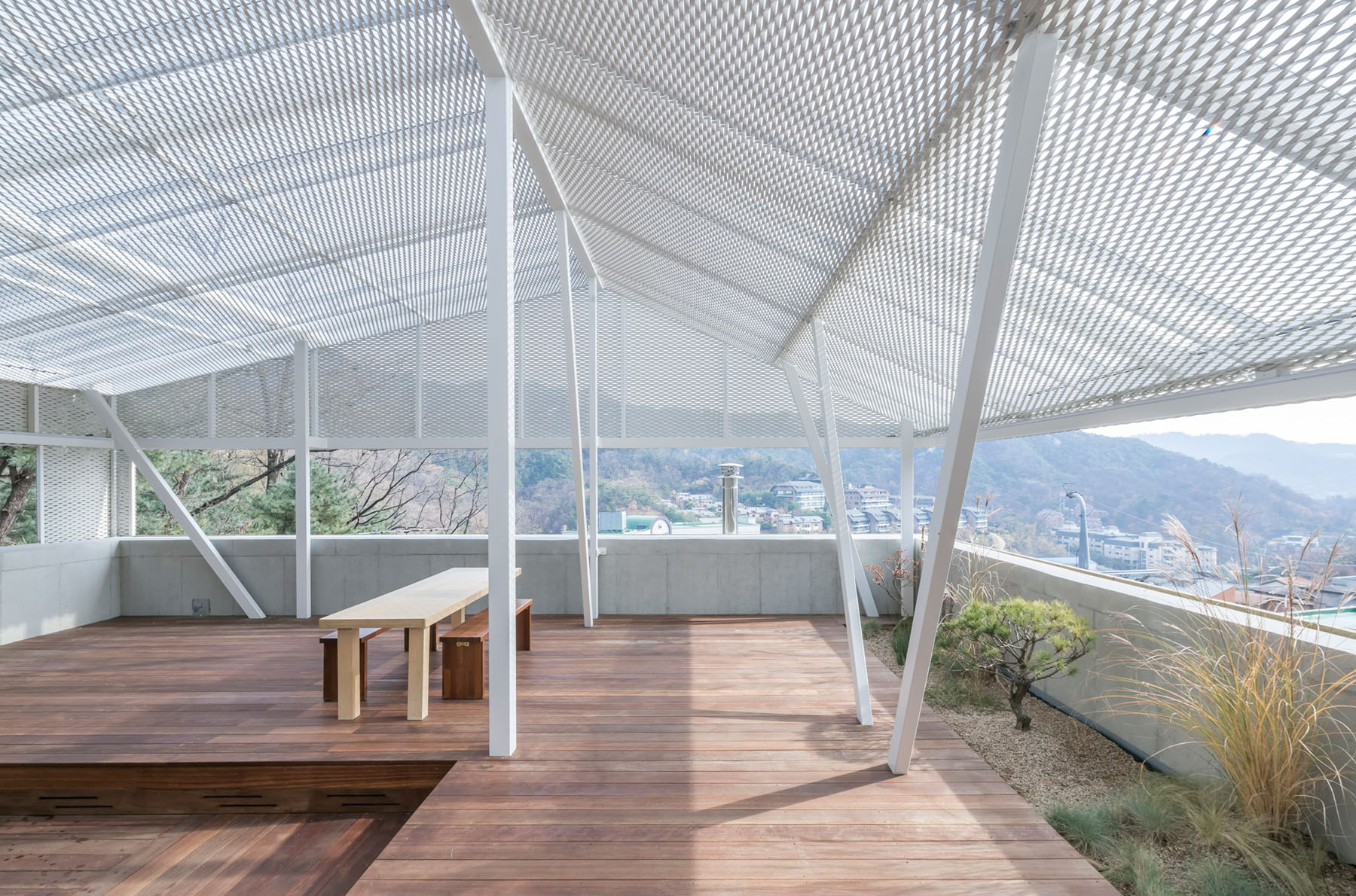 The Shaded Rooftop House by BCHO Architects — A rooftop terrace in Seoul photographed during daylight, featuring a white steel post-and-beam frame supporting a perforated metal mesh ceiling with gridded...