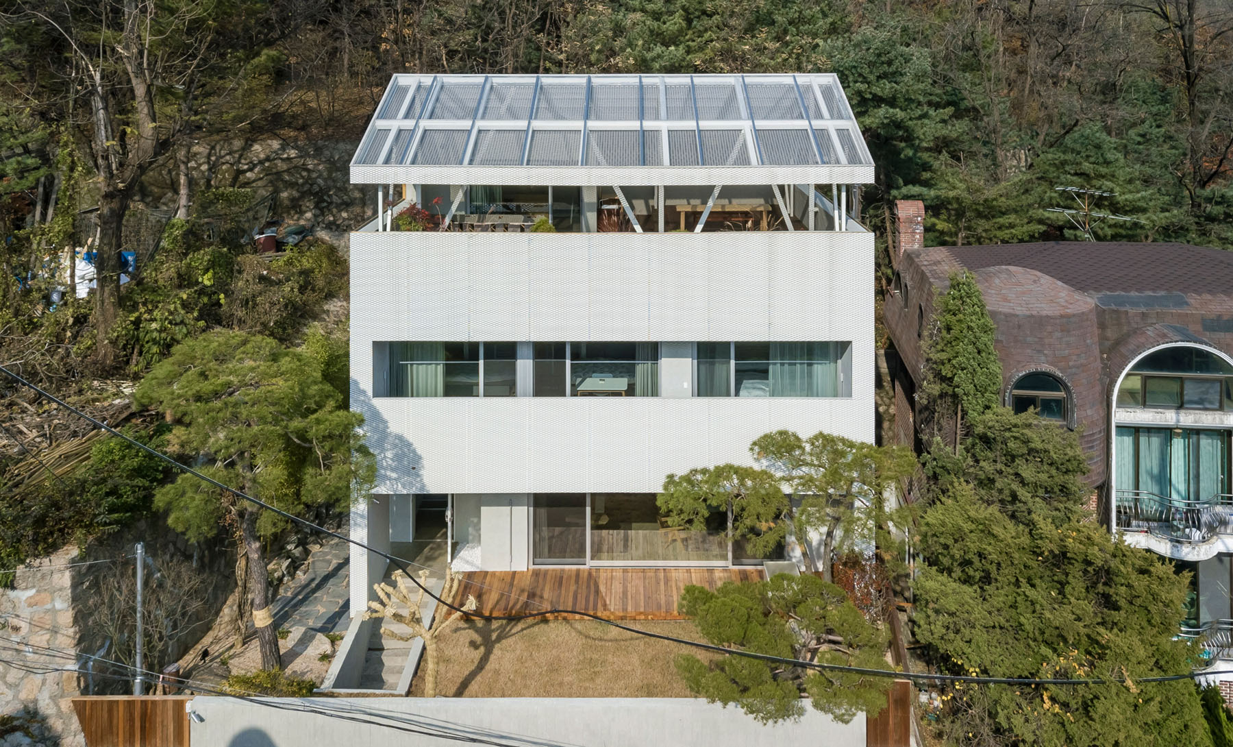 The Shaded Rooftop House by BCHO Architects — Aerial view of a three-story residential structure with a distinctive gridded rooftop system.