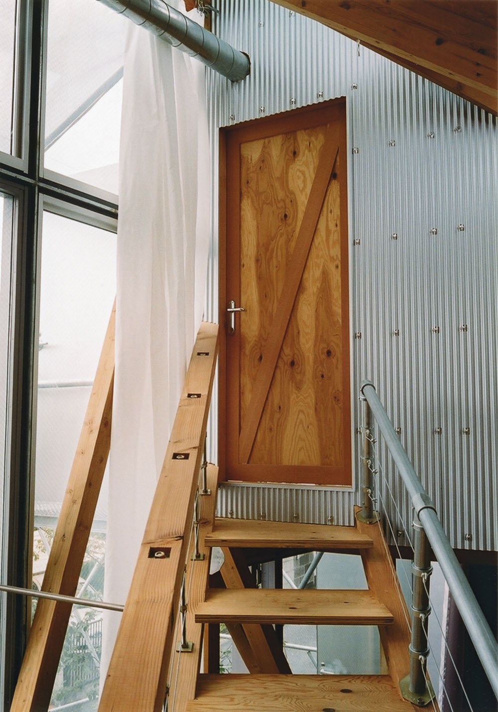 Daita2019 House by Suzuko Yamada Architects — A wooden staircase ascends toward a timber door set within an industrial framework of corrugated metal cladding.