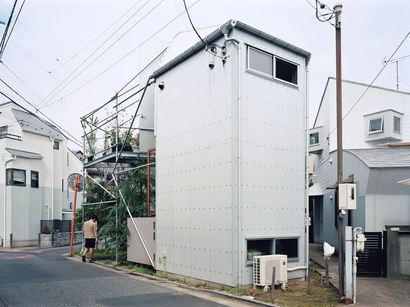 Daita2019 House by Suzuko Yamada Architects — A white-rendered corrugated metal facade dominates this street-facing elevation of the Daita2019 House, its monolithic surface punctuated by a single...