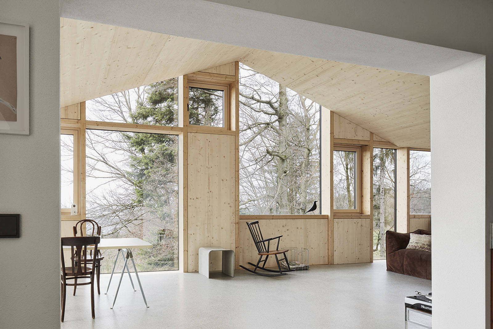 House Hohlen by Jochen Specht — Interior view of the House Hohlen showing the expansive glazed envelope framing a winter landscape of bare deciduous trees and evergreen conifers.