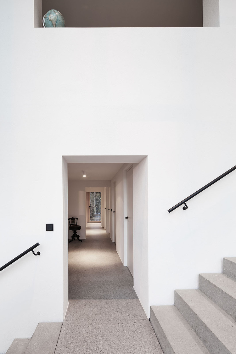 House Hohlen by Jochen Specht — A corridor perspective reveals the spatial progression through House Hohlen's interior, with concrete steps descending on the right and black-painted steel...