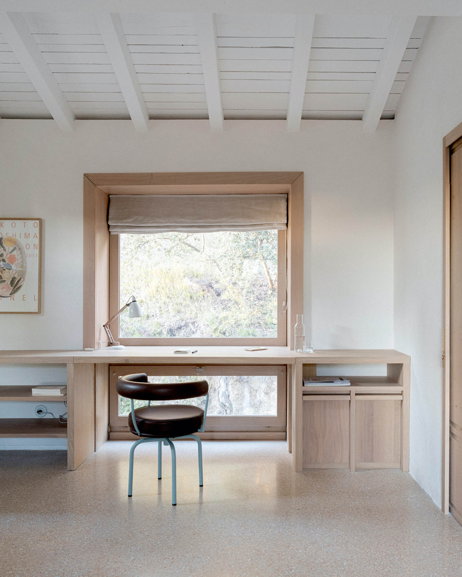 MA House by Studio XM — Interior workspace positioned within the home's wooden-framed structure, featuring a light oak desk built-in beneath a large window with roller shade.