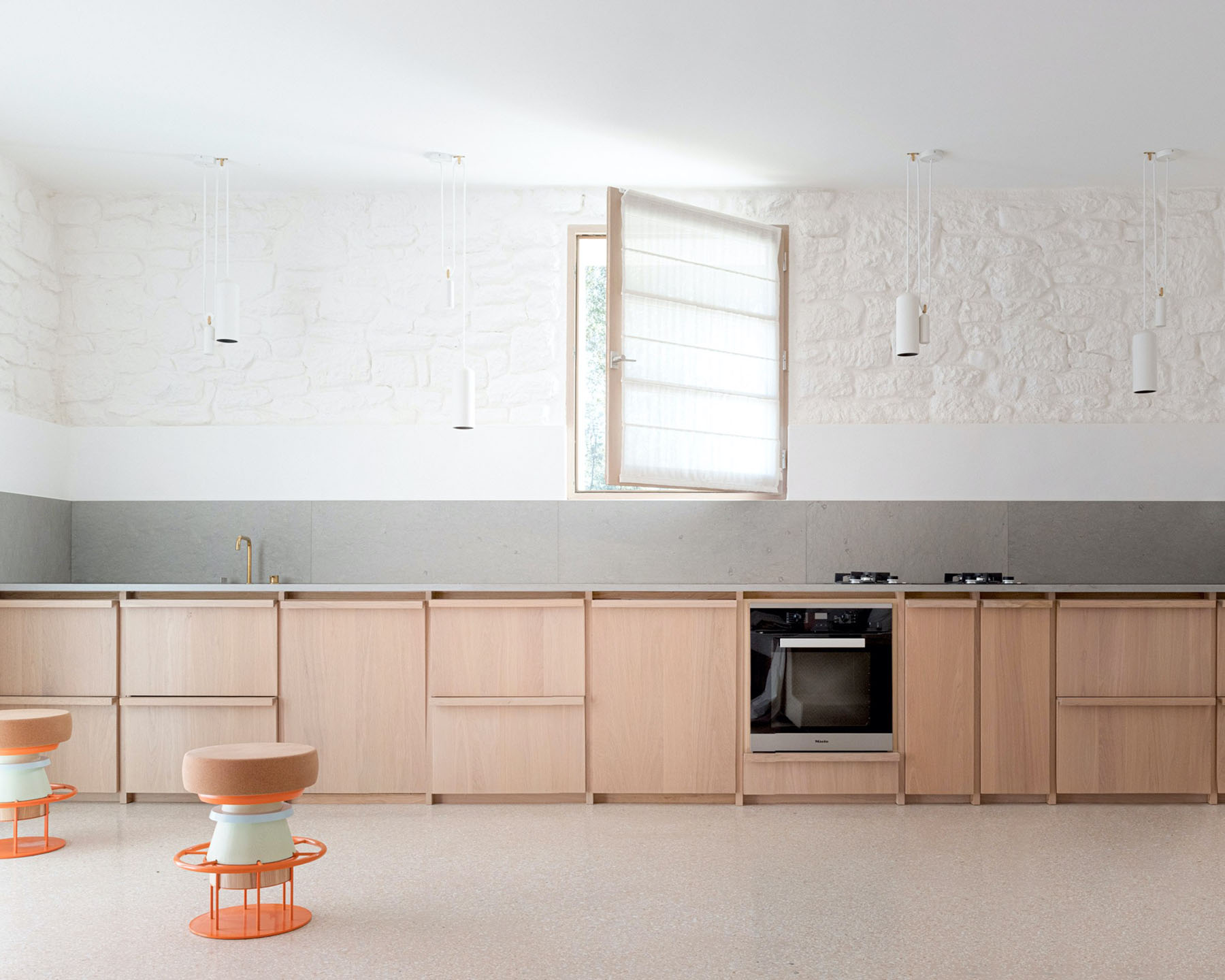 MA House by Studio XM — Interior view of the kitchen featuring a continuous run of light timber cabinetry with recessed panel detailing beneath a polished concrete countertop.