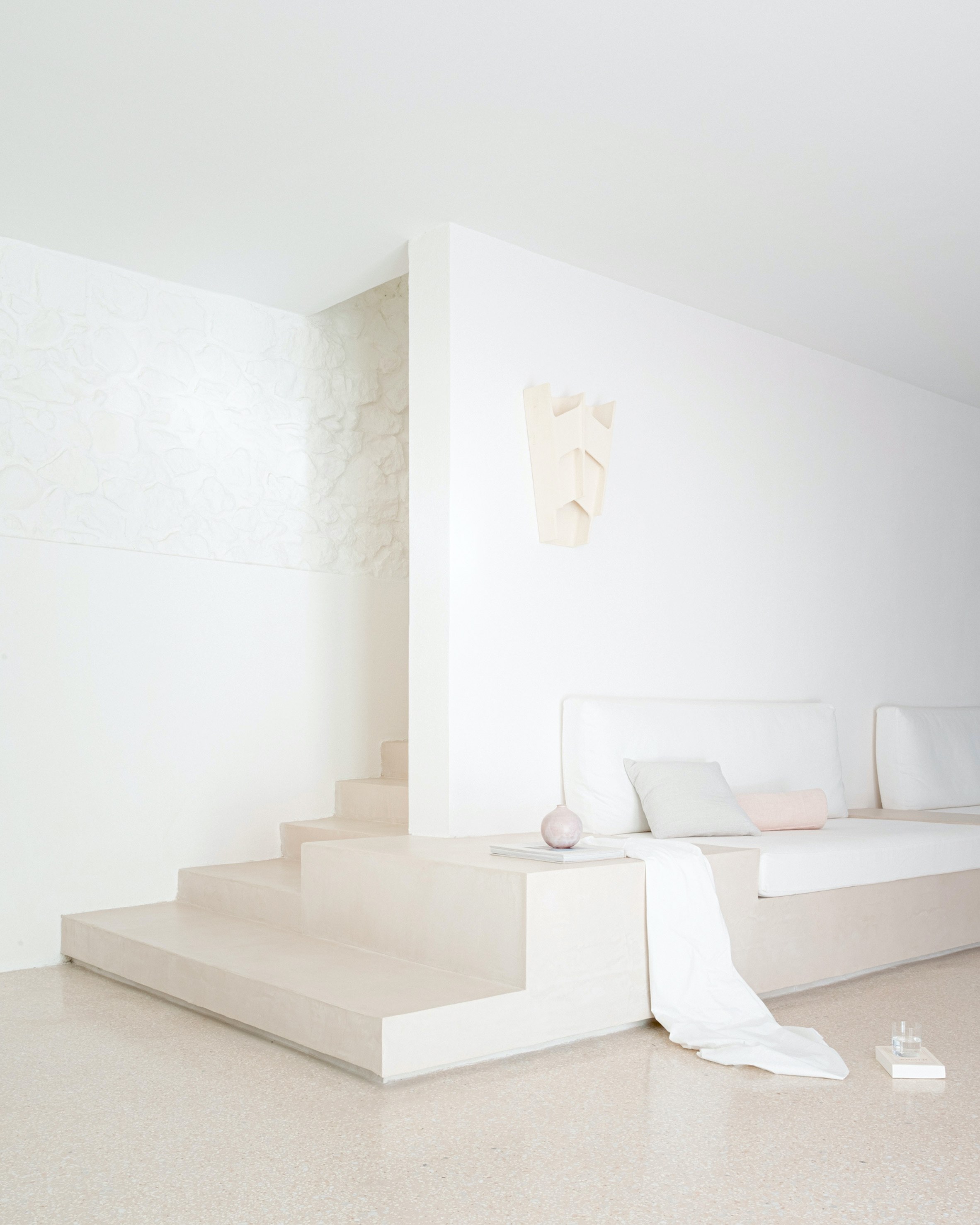 MA House by Studio XM — Interior view of MA House showing a minimalist bedroom platform accessed by shallow steps in cream-toned stone.