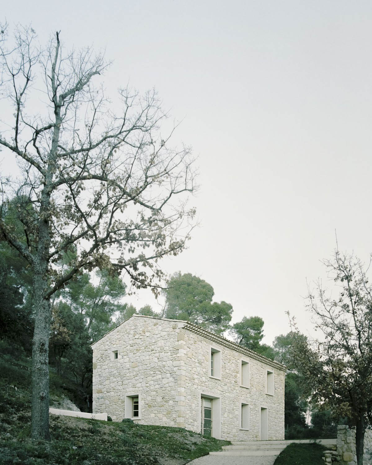 MA House by Studio XM — MA House presents a geometric stone volume set within dense woodland terrain.