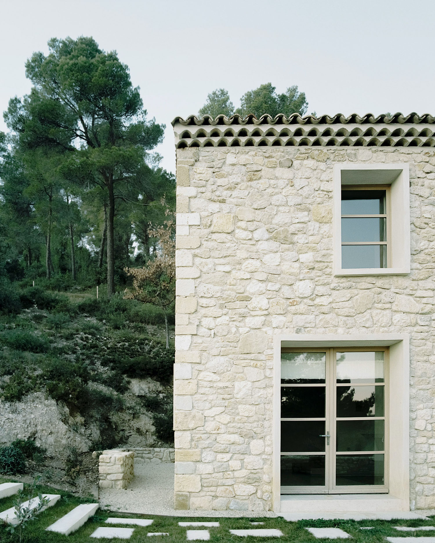 MA House by Studio XM — Studio XM's renovation of a rural Vaucluse farmhouse presents a coursed ashlar stone facade in warm cream-beige tones, anchored by regular rectangular...
