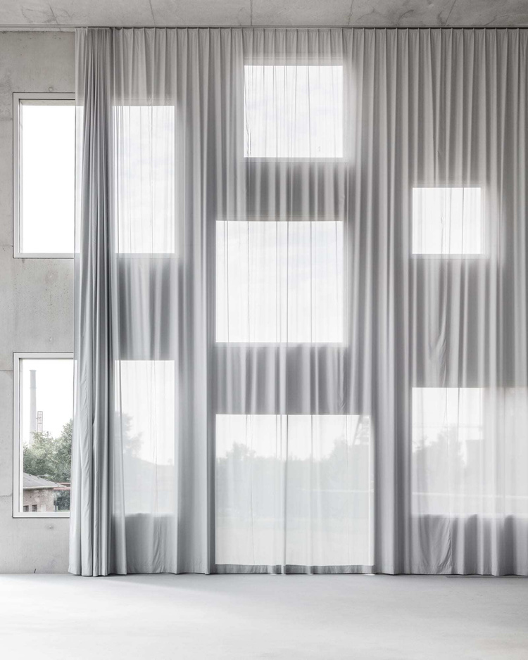 Zollverein School of Management and Design by SANAA — Floor-to-ceiling sheer curtains suspend across the studio interior, their vertical pleats casting graduated shadow patterns onto the concrete wall behind.