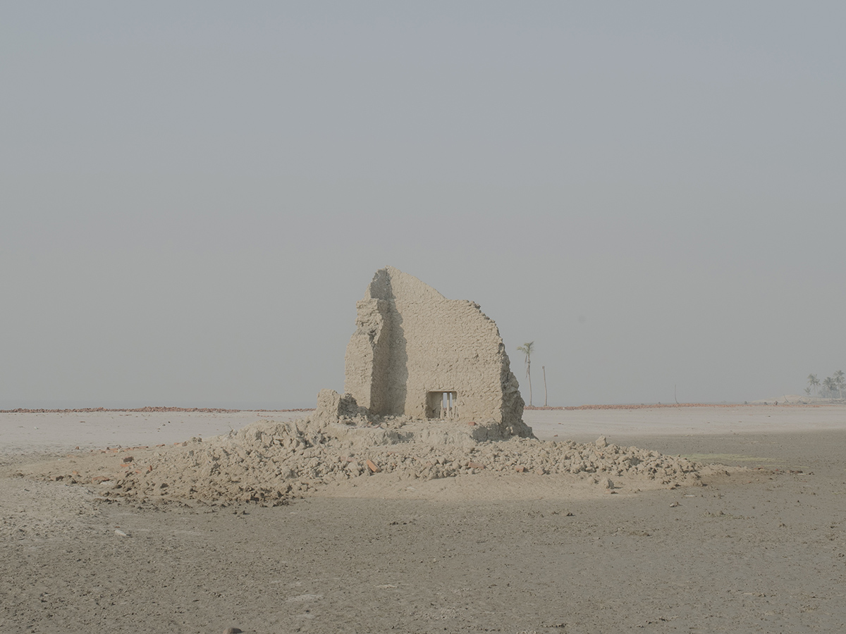 Ebbing away of Identity with the Tides by Sushavan Nandy — A deteriorating concrete structure stands isolated in the Sundarbans landscape, its monolithic form partially obscured by accumulated rubble and sediment.