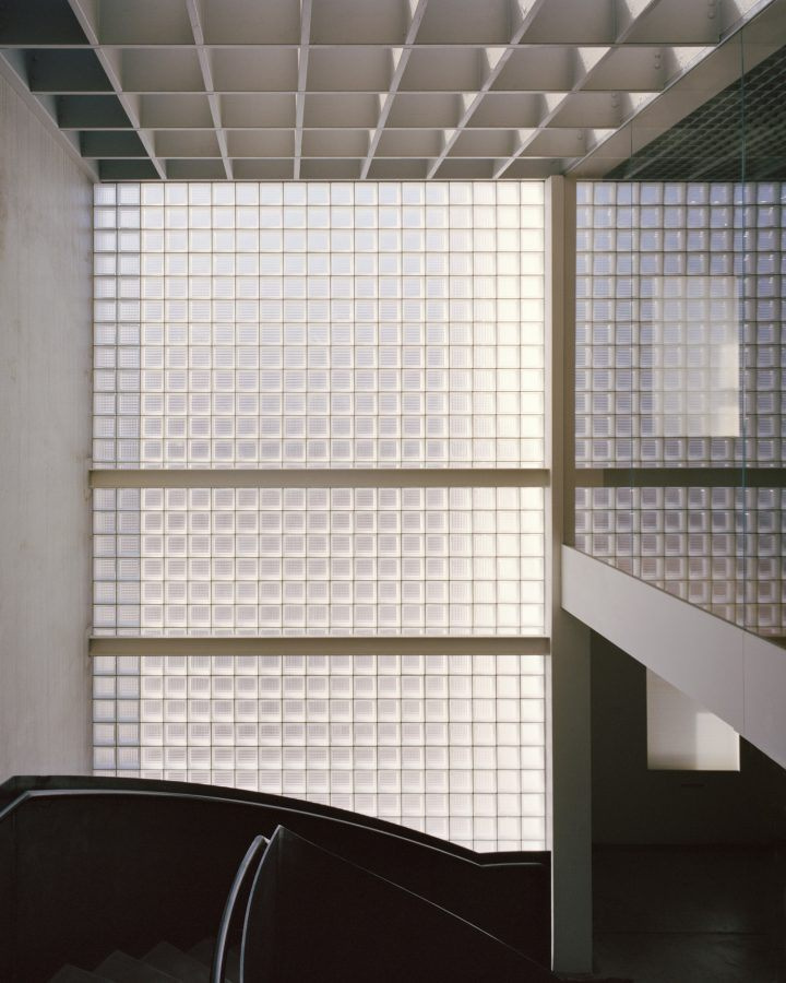 Yoga Studio by Richard Stampton — A stairwell descends into the yoga studio's atrium, where a curved black steel form creates stark geometric contrast against the overhead gridded ceiling.