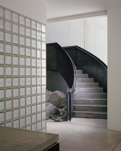 Yoga Studio by Richard Stampton — A curved black steel staircase descends into the atrium space, its sculptural form contrasting sharply against the bright overhead gridded glass panels.