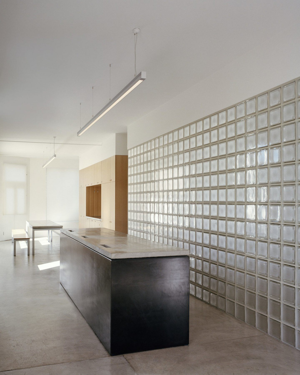 Yoga Studio by Richard Stampton — A linear black steel counter bisects the studio's ground plane, its dark monolithic form anchoring the composition against a backdrop of gridded translucent...