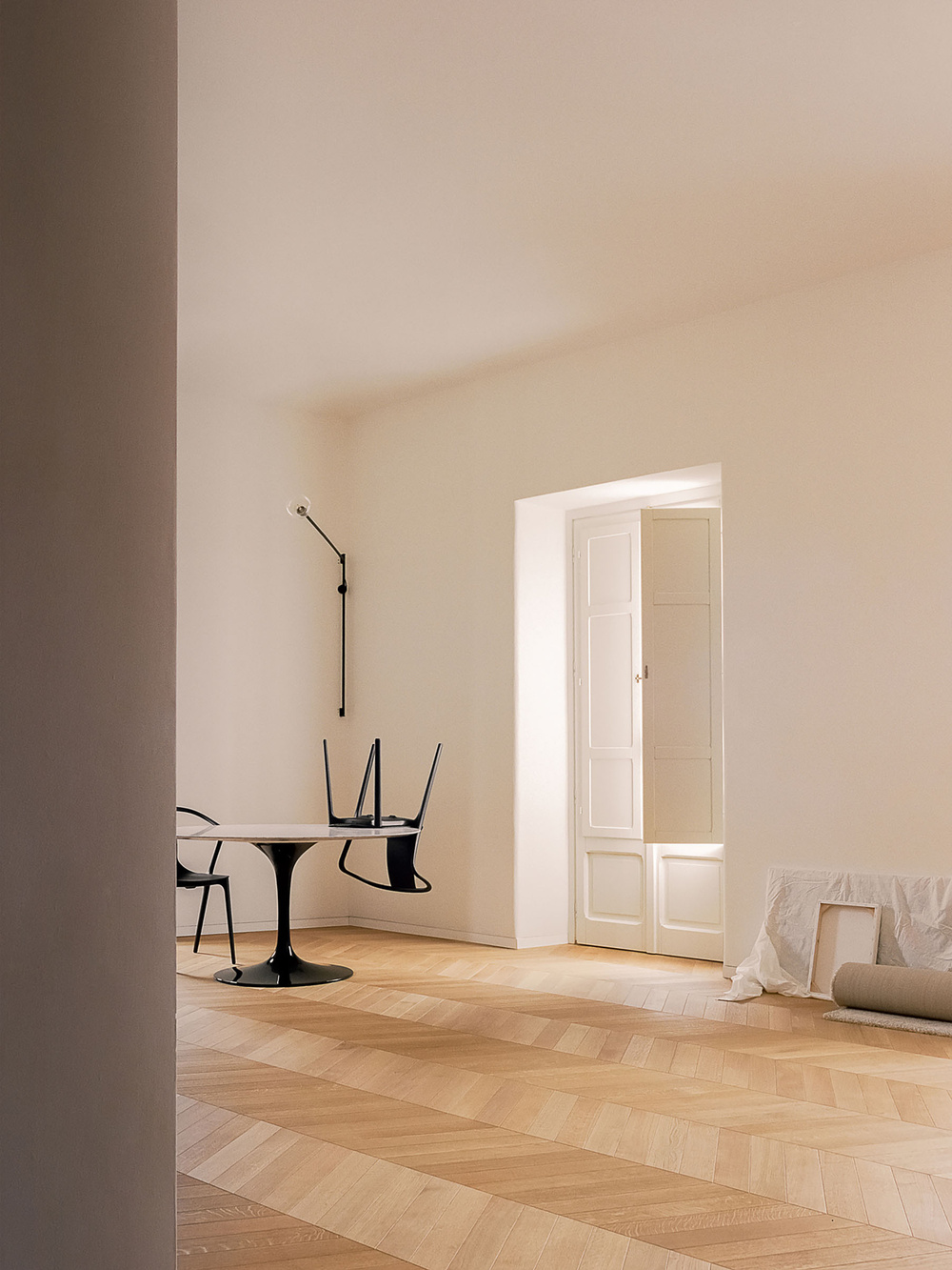 House for a Couple by SET Architects — A sparsely furnished corner of the renovated apartment features herringbone oak flooring in warm honey tones, establishing directional rhythm across the space.