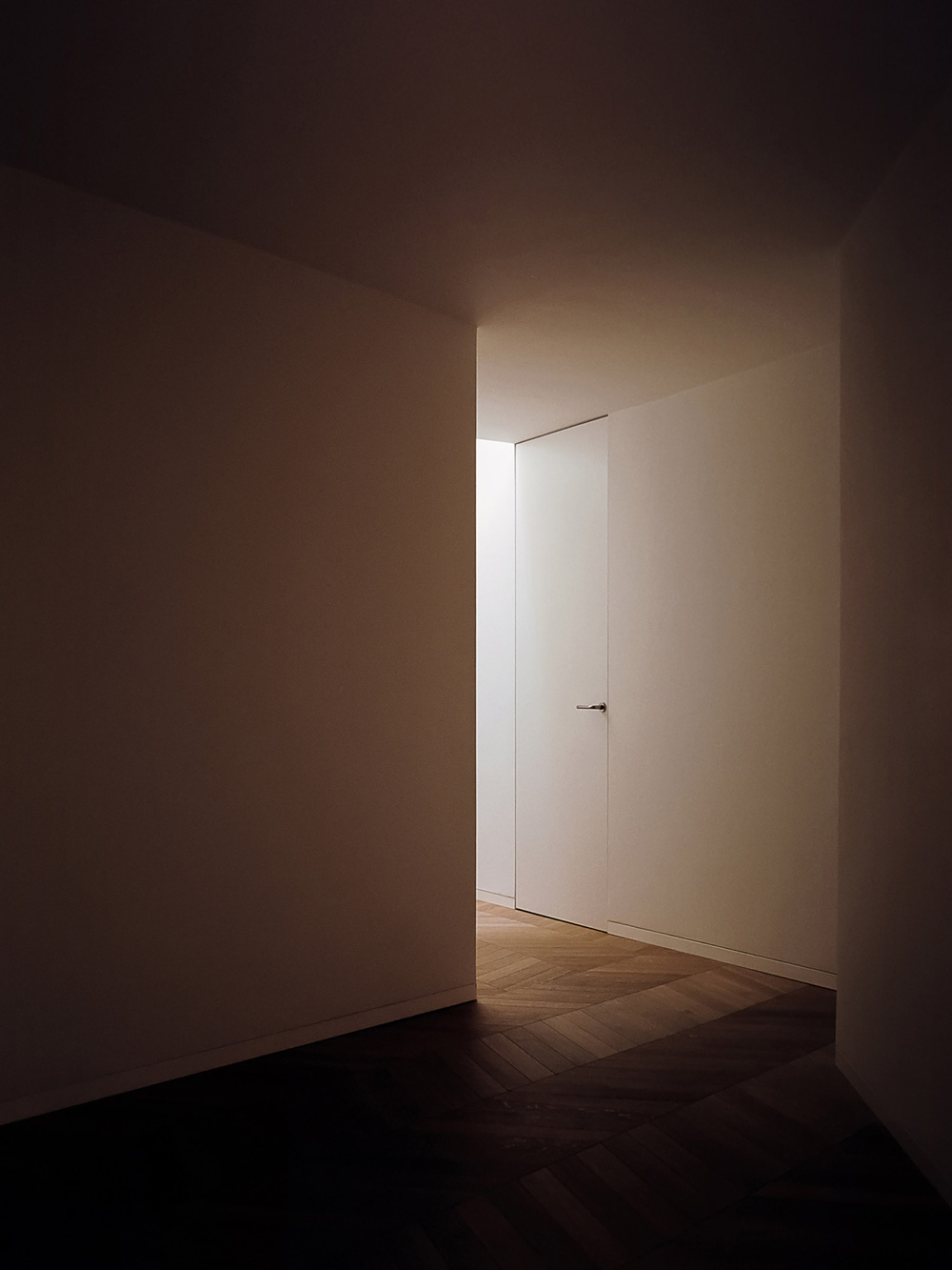 House for a Couple by SET Architects — A view through an open white paneled double door frames a threshold into an adjacent room with herringbone oak flooring.