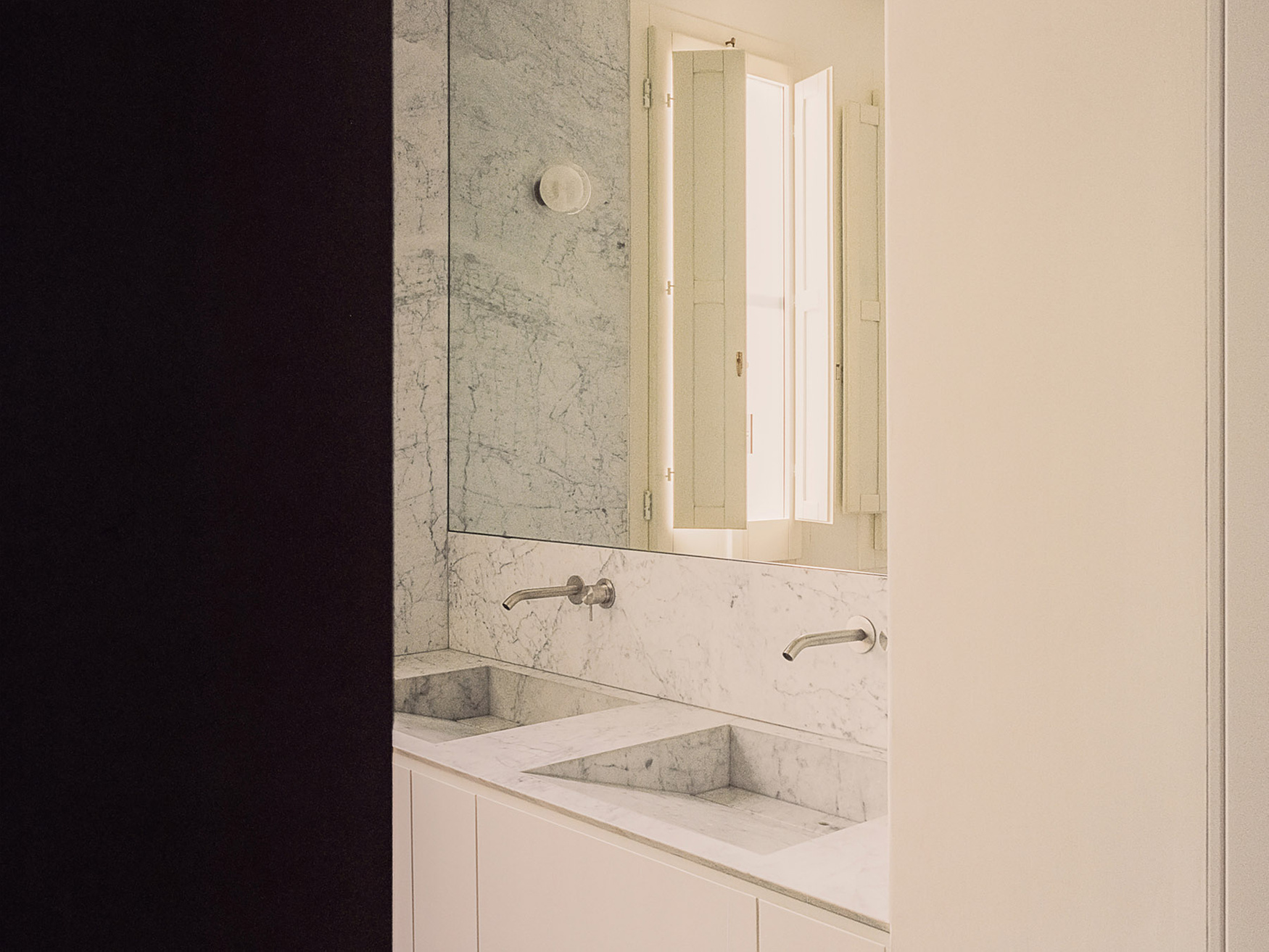 House for a Couple by SET Architects — A bathroom vanity in marble showcases dual rectangular basins carved from a single slab, with brushed metal wall-mounted faucets positioned asymmetrically.