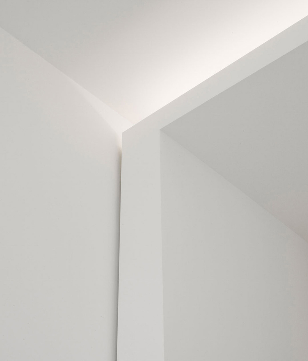 Alkema Studio by Jen Alkema Architect — A vertical light slot bisects two monolithic white wall planes, creating a threshold effect between interior spaces.