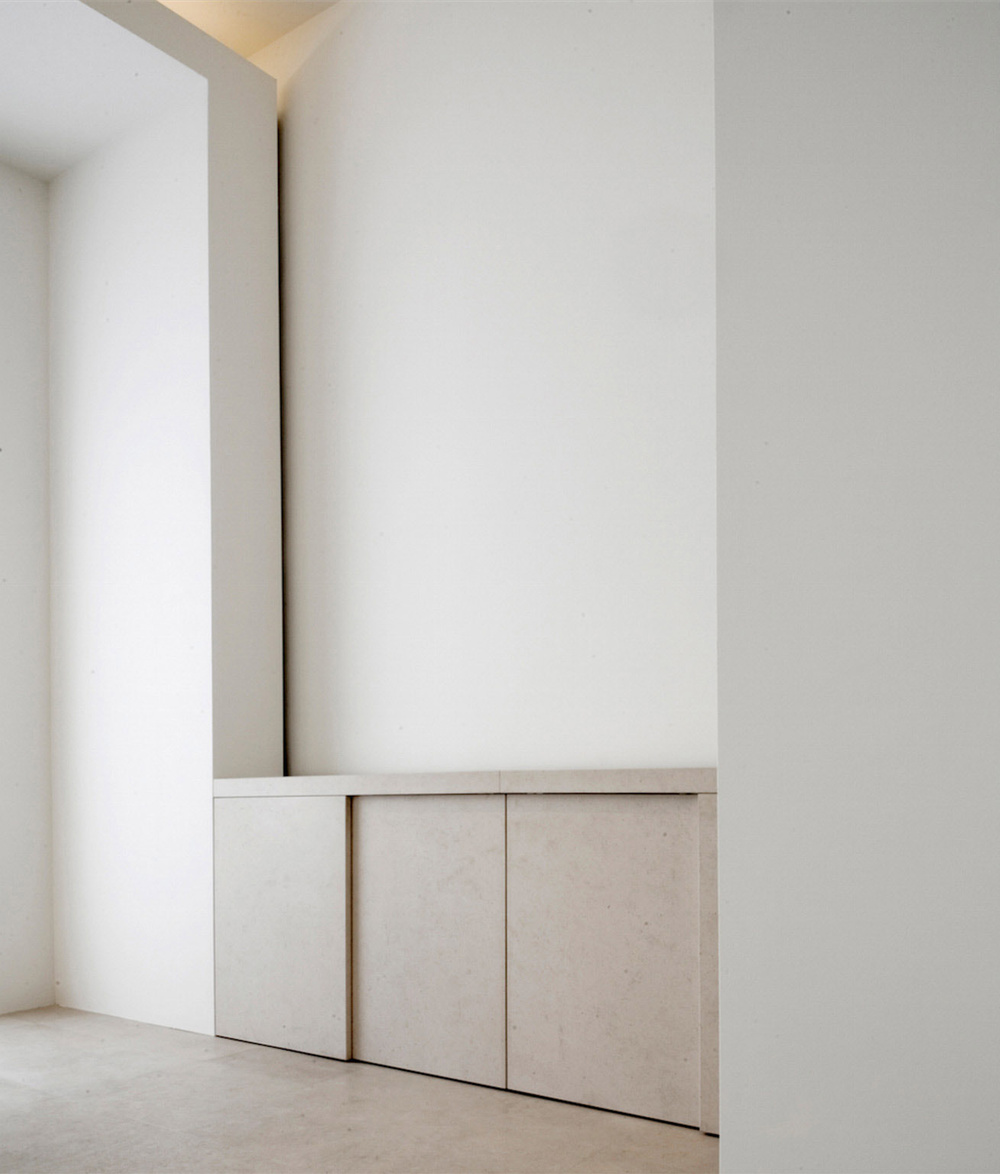Alkema Studio by Jen Alkema Architect — A minimalist interior passage features a monolithic wall panel with subtle horizontal divisions bisecting the composition.