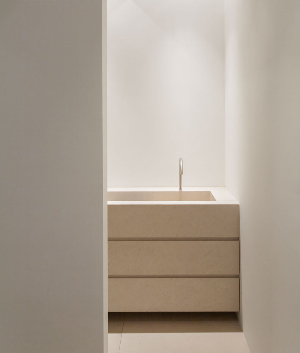 Alkema Studio by Jen Alkema Architect — A minimalist bathroom alcove features a floating timber vanity with three horizontal drawer divisions in a warm beige tone, positioned beneath a rectangular...